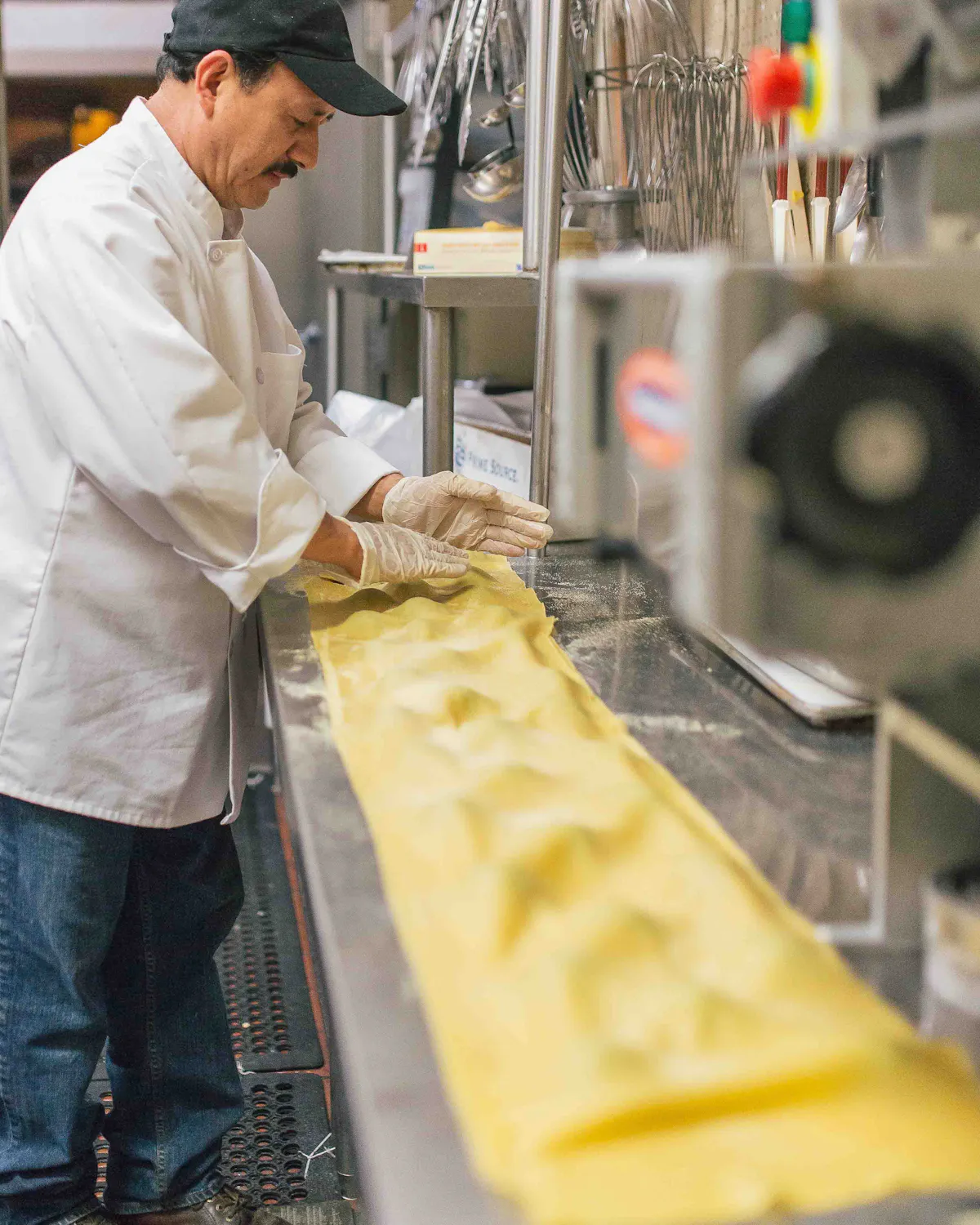 a man in a white coat and gloves making pasta