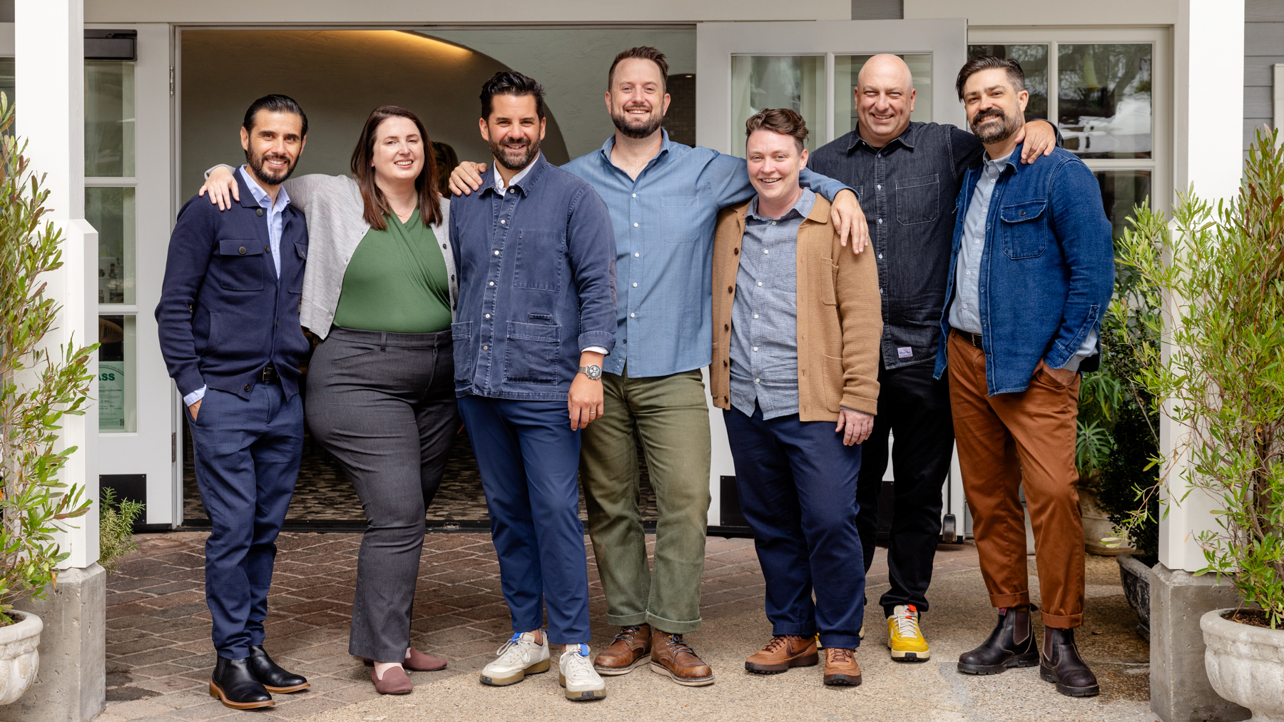 seven people stand together outside a building, posing for a group photo