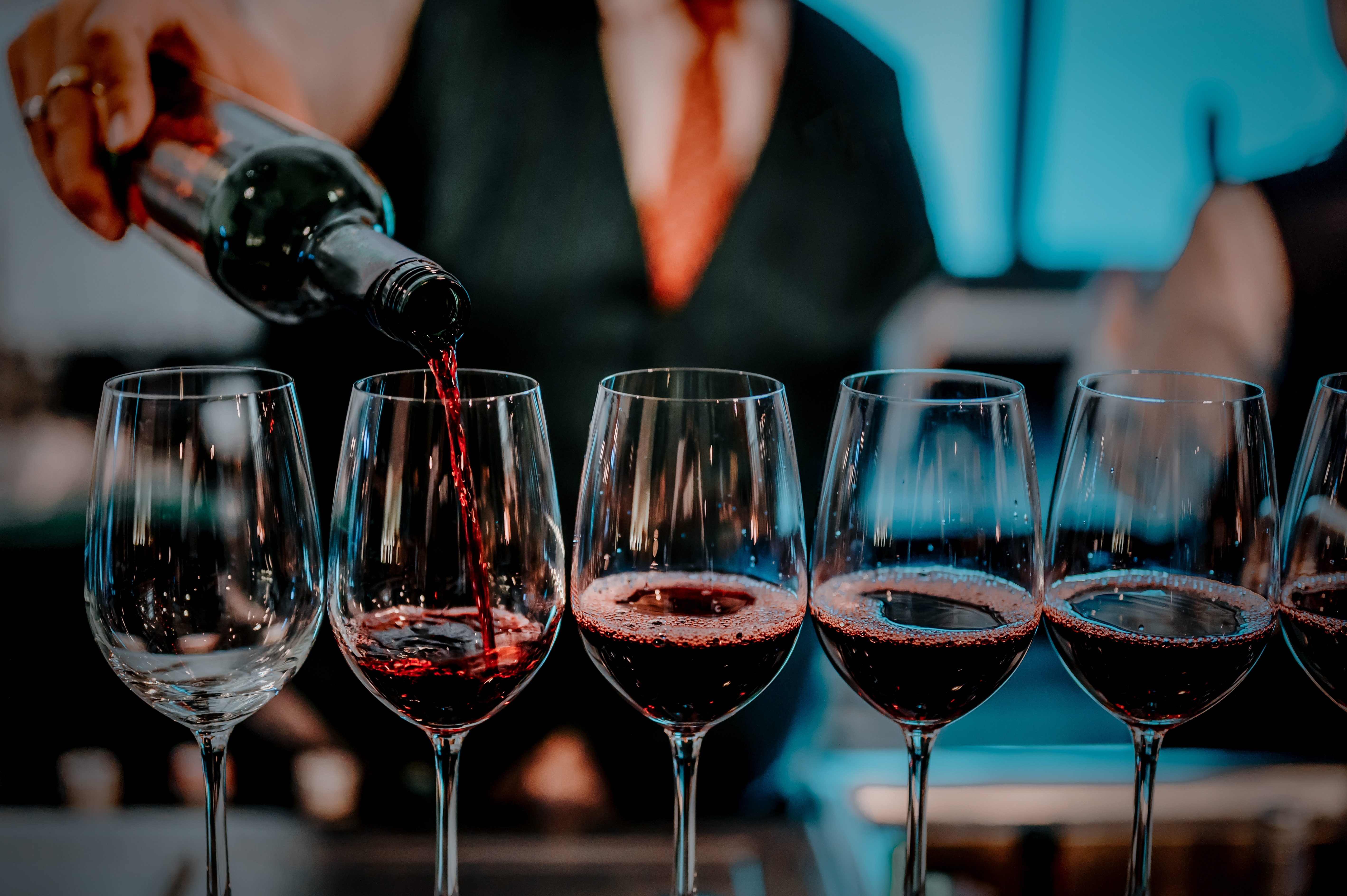 a person pouring wine into a row of wine glasses