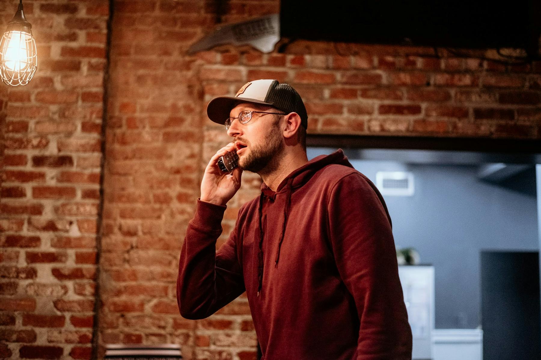 a man standing in front of a brick wall talking on a cell phone