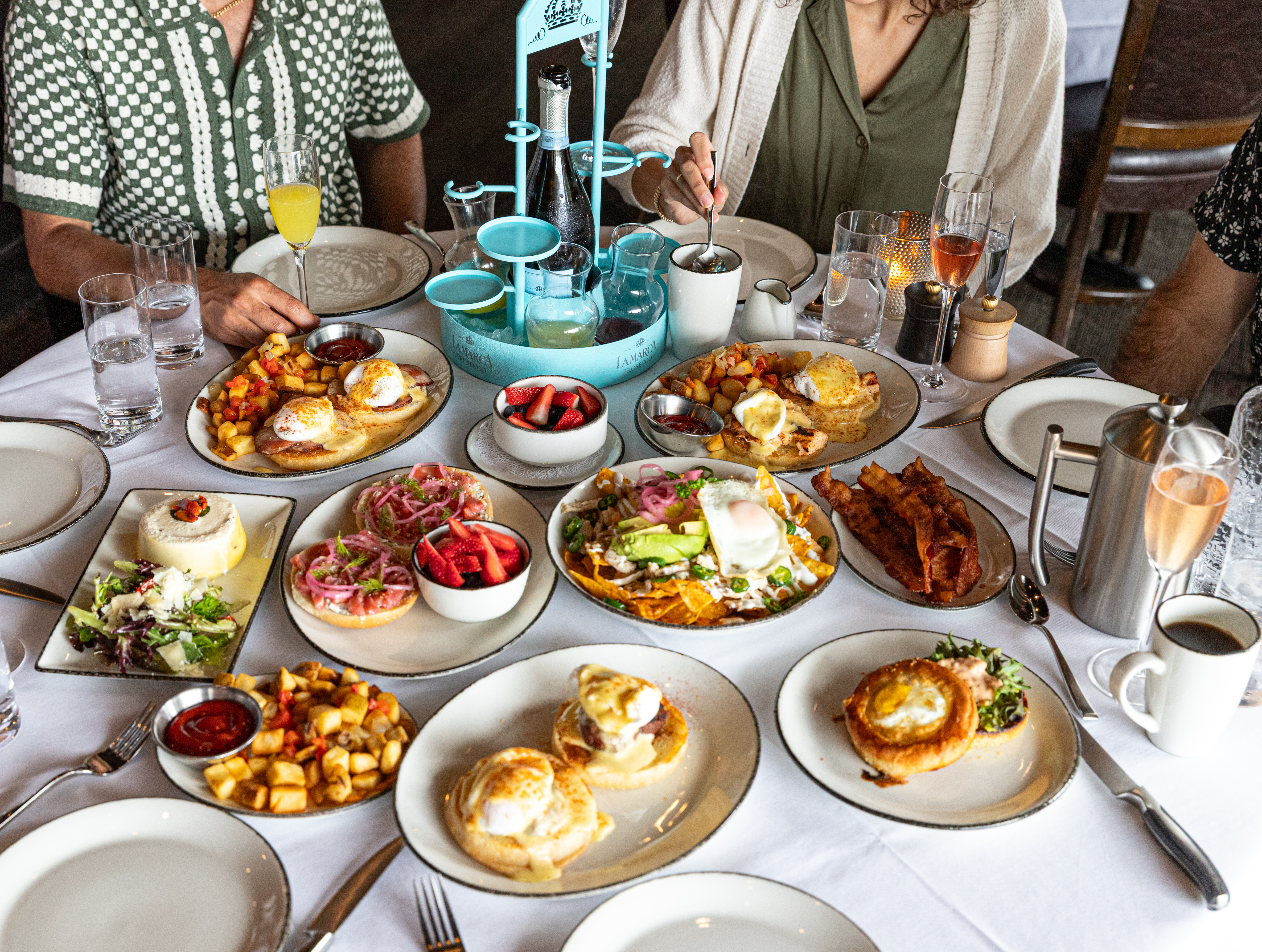 Table full of brunch items: eggs benedict, hash browns, breakfast sliders, mimosas.
