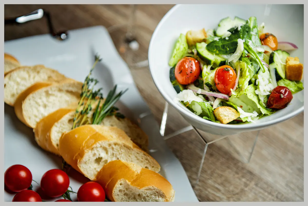 two plates of food with bread and a salad served in bowl. 