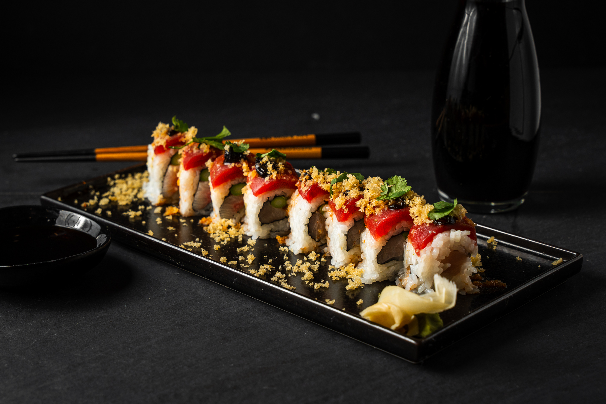a plate of sushi with chopsticks and a glass of soy sauce