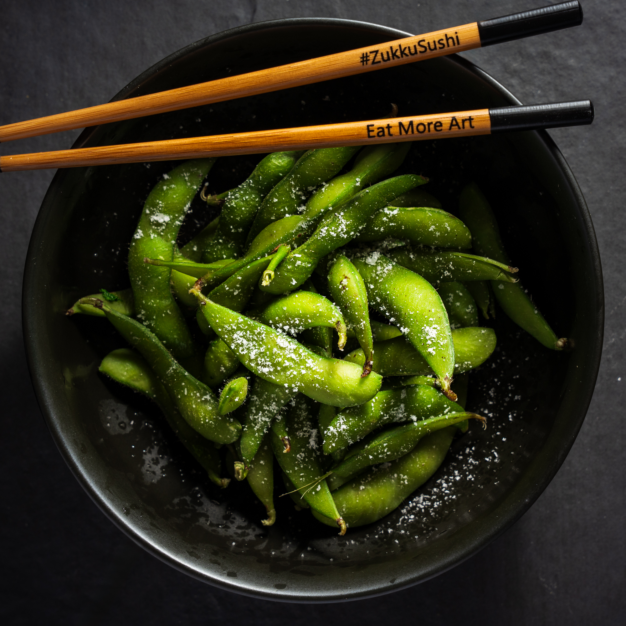 a bowl of green peas with chopsticks