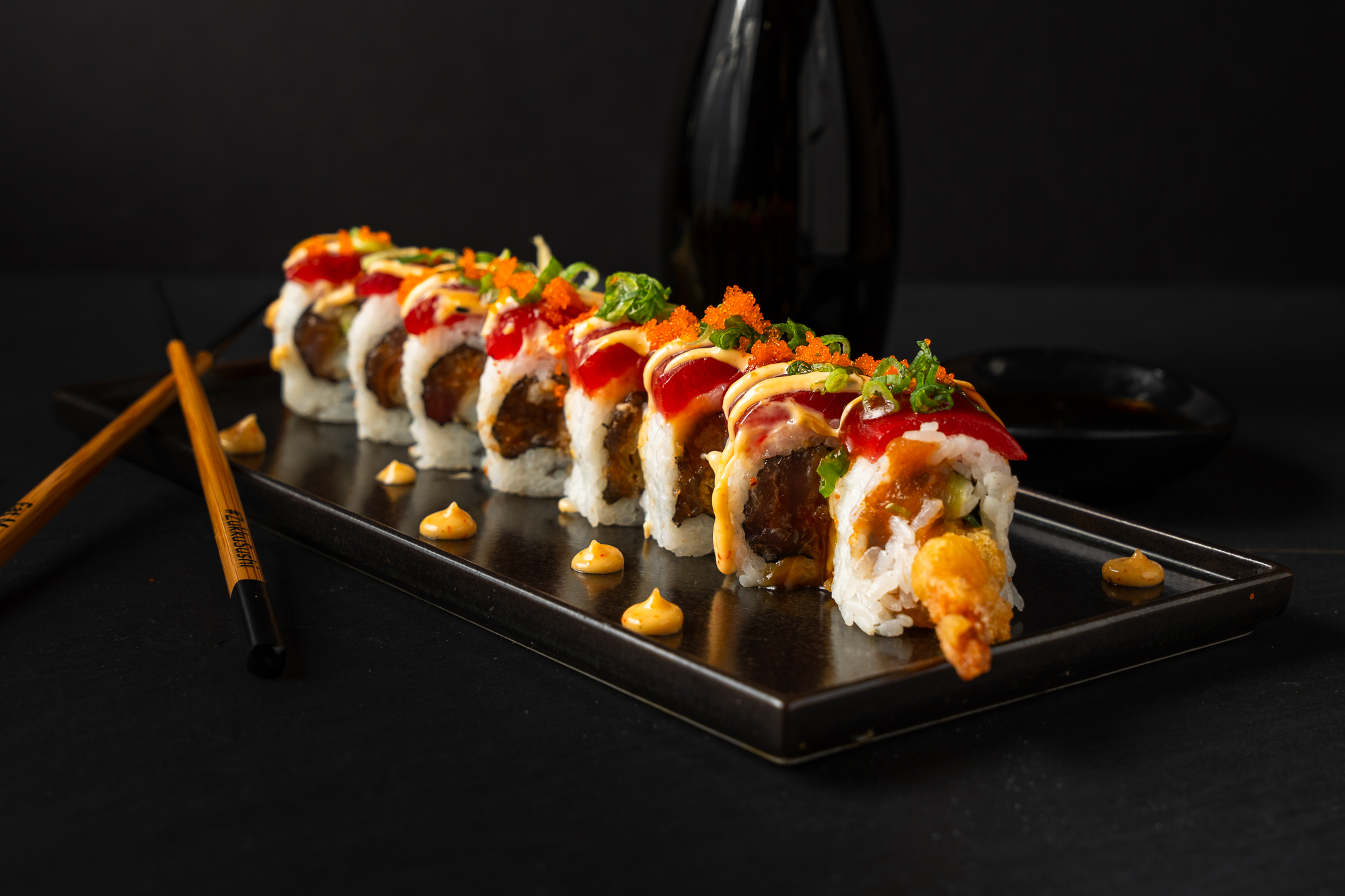 a plate of sushi with chopsticks and a bottle