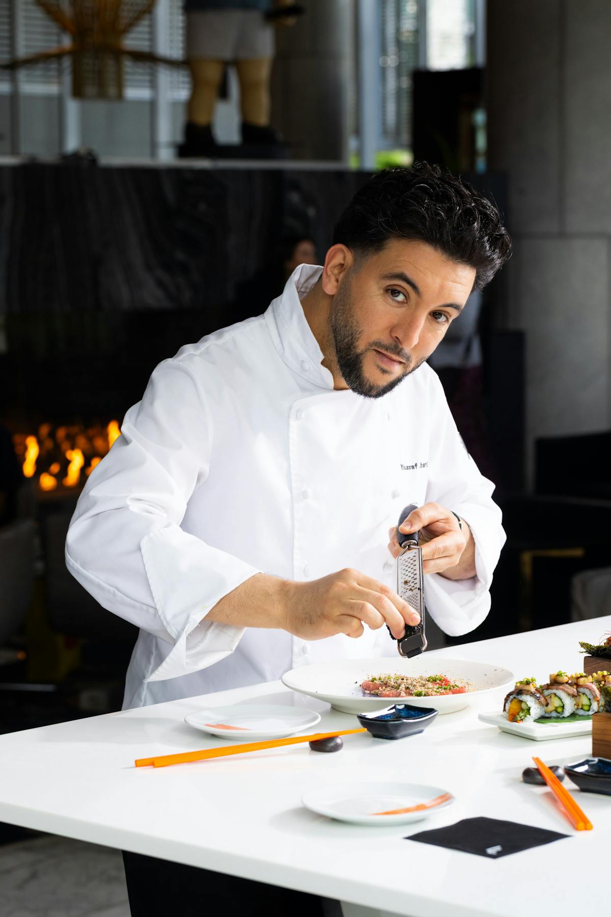Chef Youssef Jbari of The Lobby Lounge & RawBar grating truffle onto a plate of food with a fireplace in the background