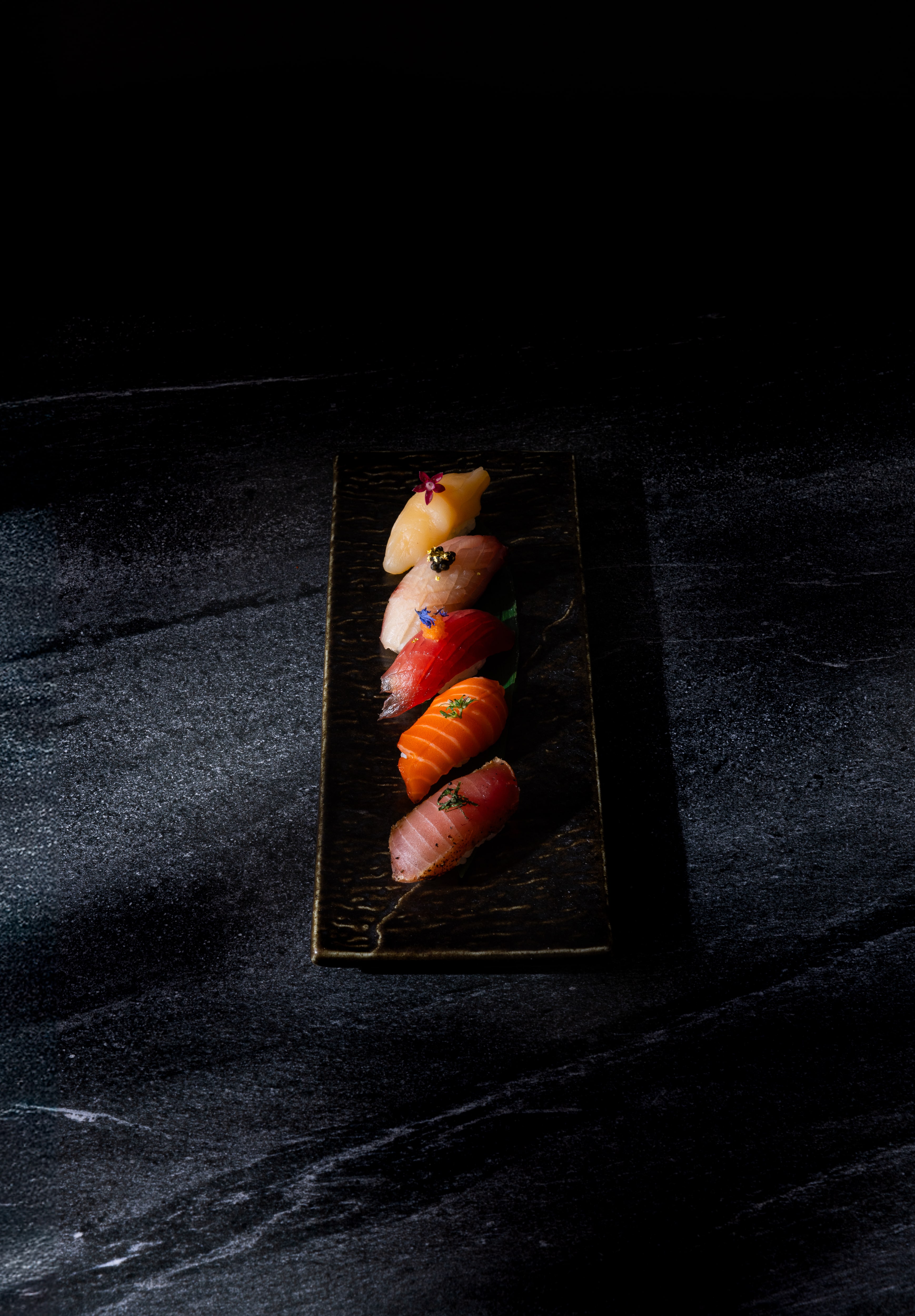 A row of five pieces of sushi on a black plate