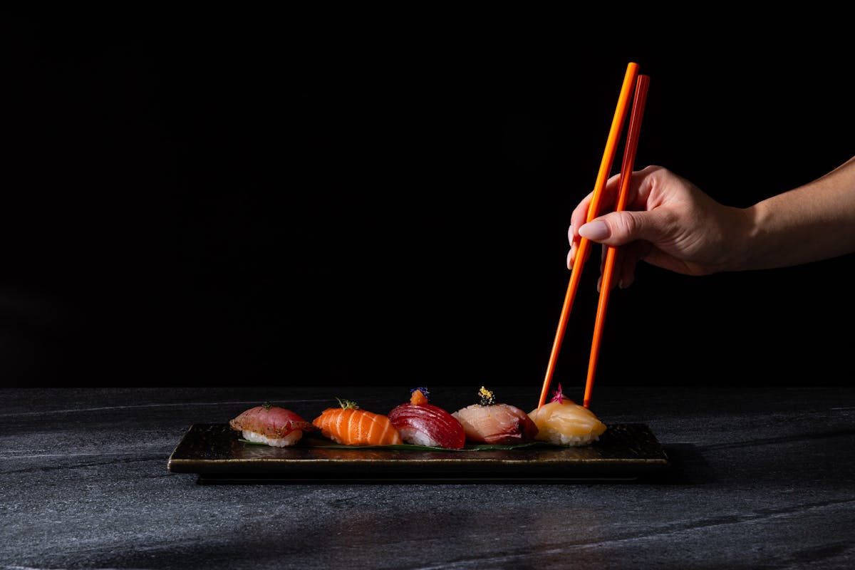 Hand holding orange chopsticks above a row of fresh sushi in Vancouver