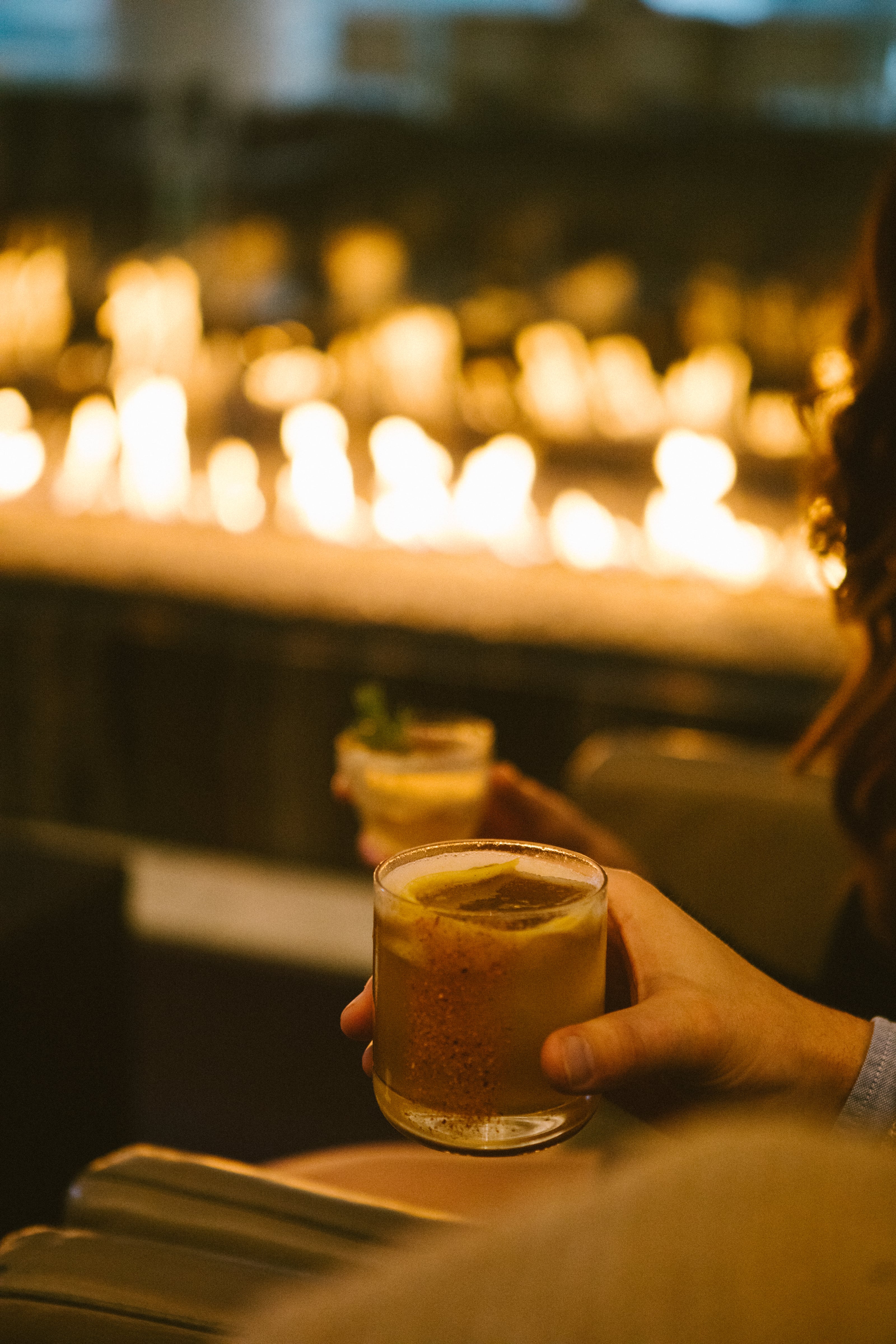 Person holding a cocktail in front of a fireplace