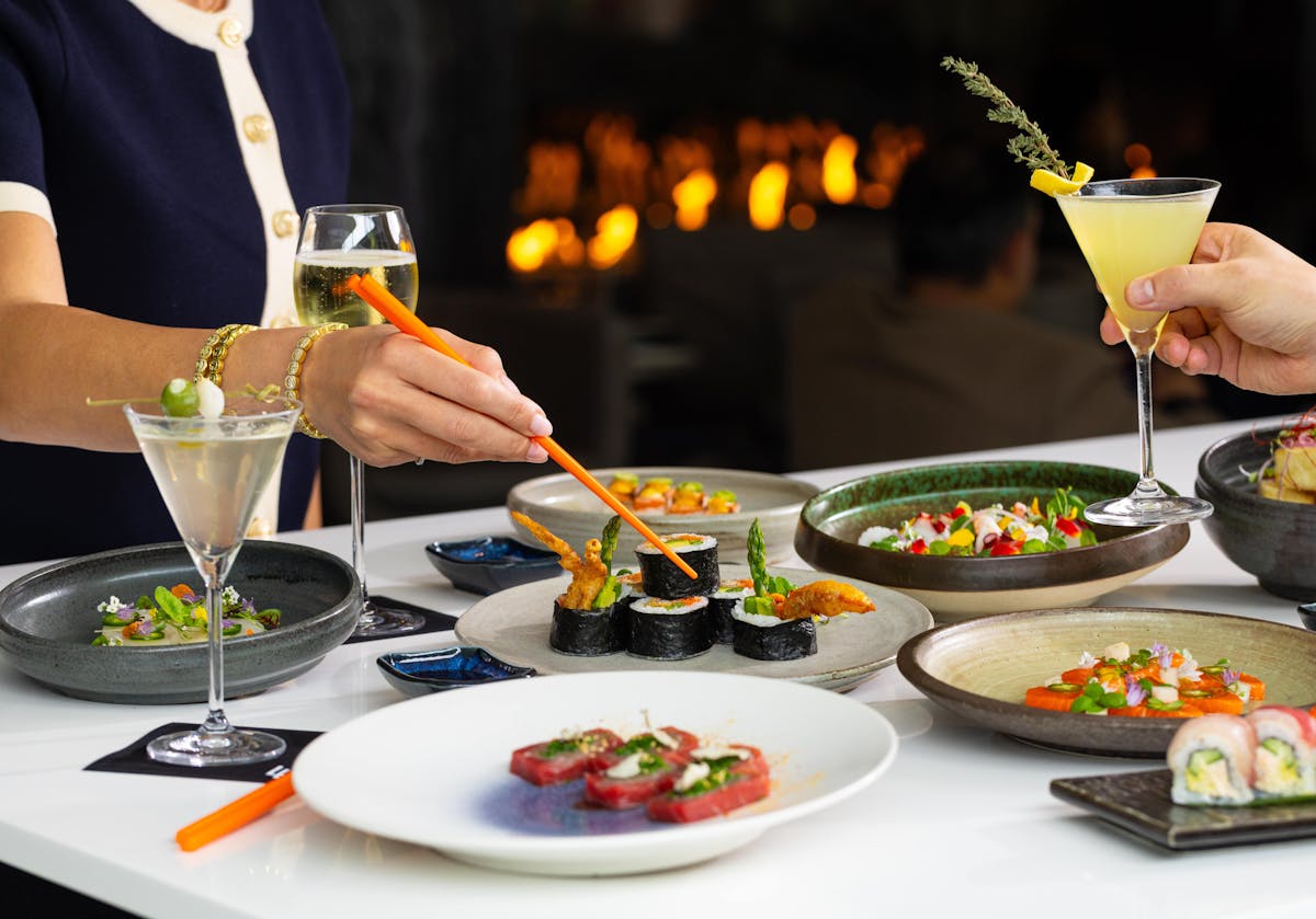 A table filled with plates of sushi and a hand using orange chopsticks to pick up sushi