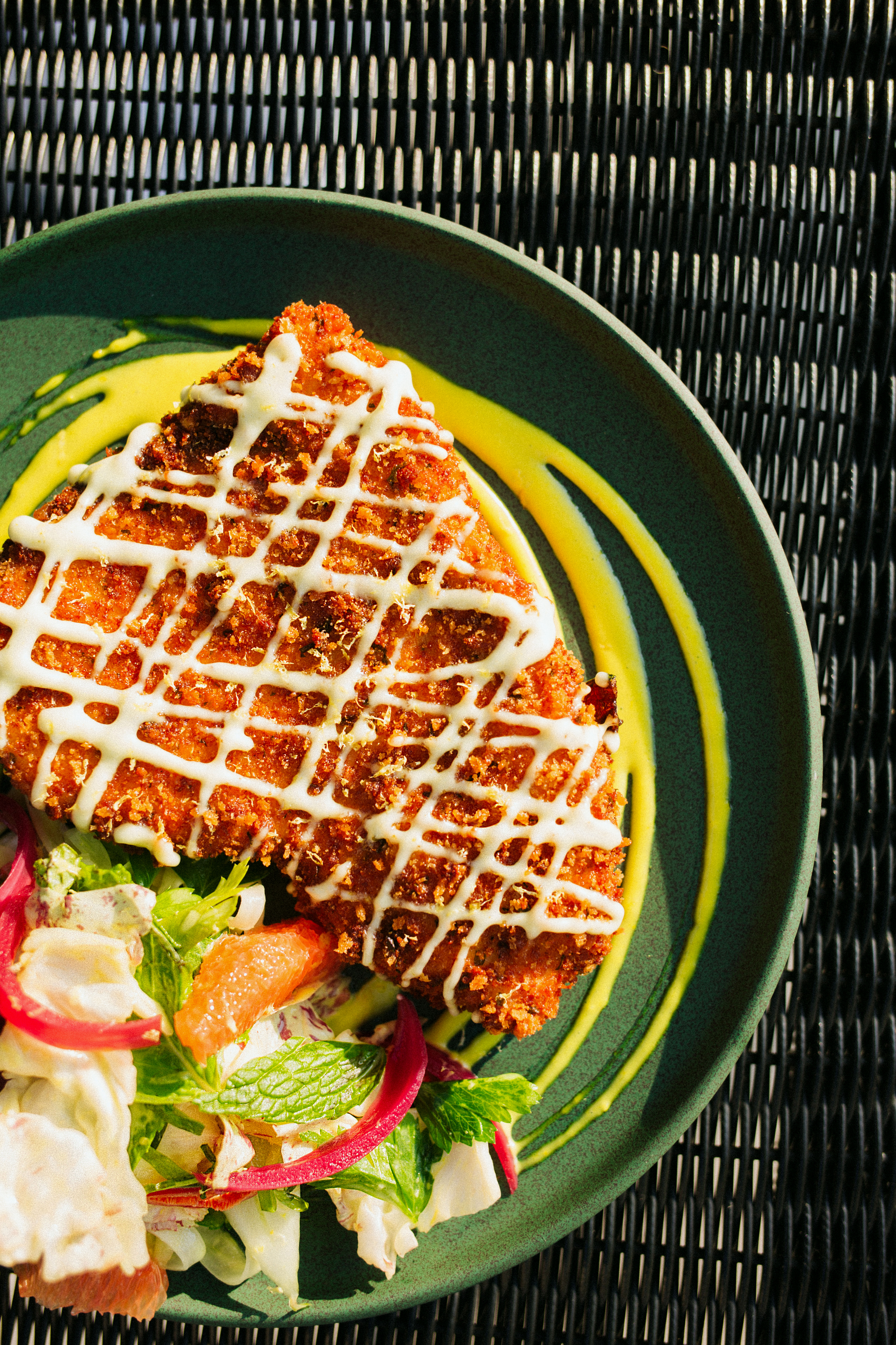 A piece of chicken on a plate with a side salad and dressing drizzled on top