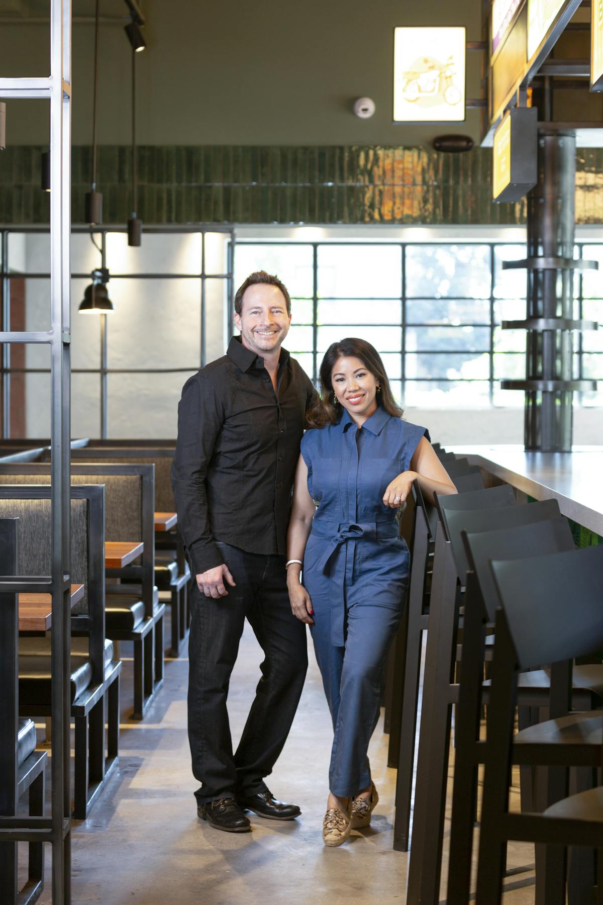 A man and woman stand together in front of a restaurant, smiling and enjoying their time outdoors