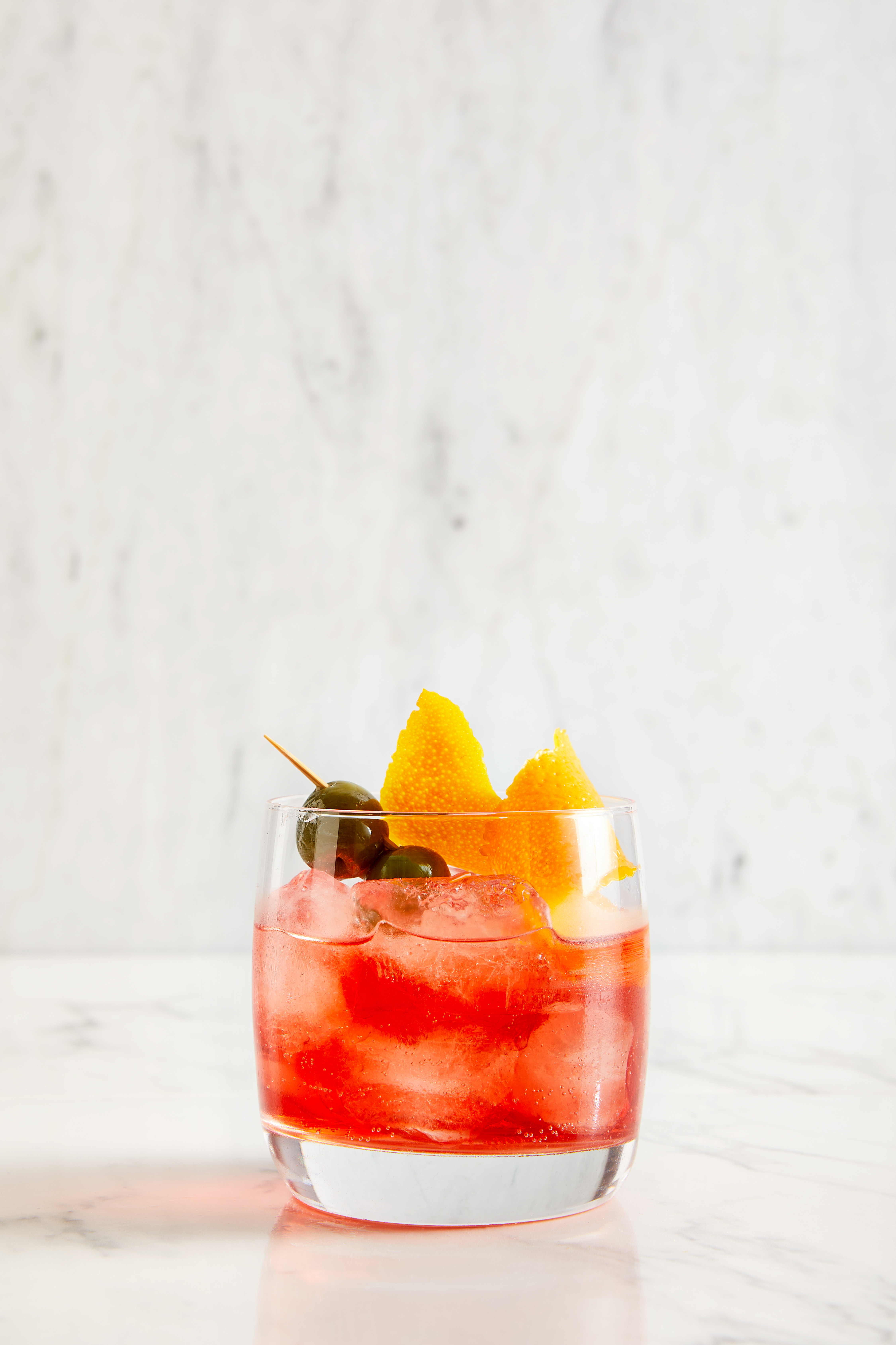 A glass of red cocktail garnished with orange slices and olives, showcasing vibrant colors and refreshing appeal