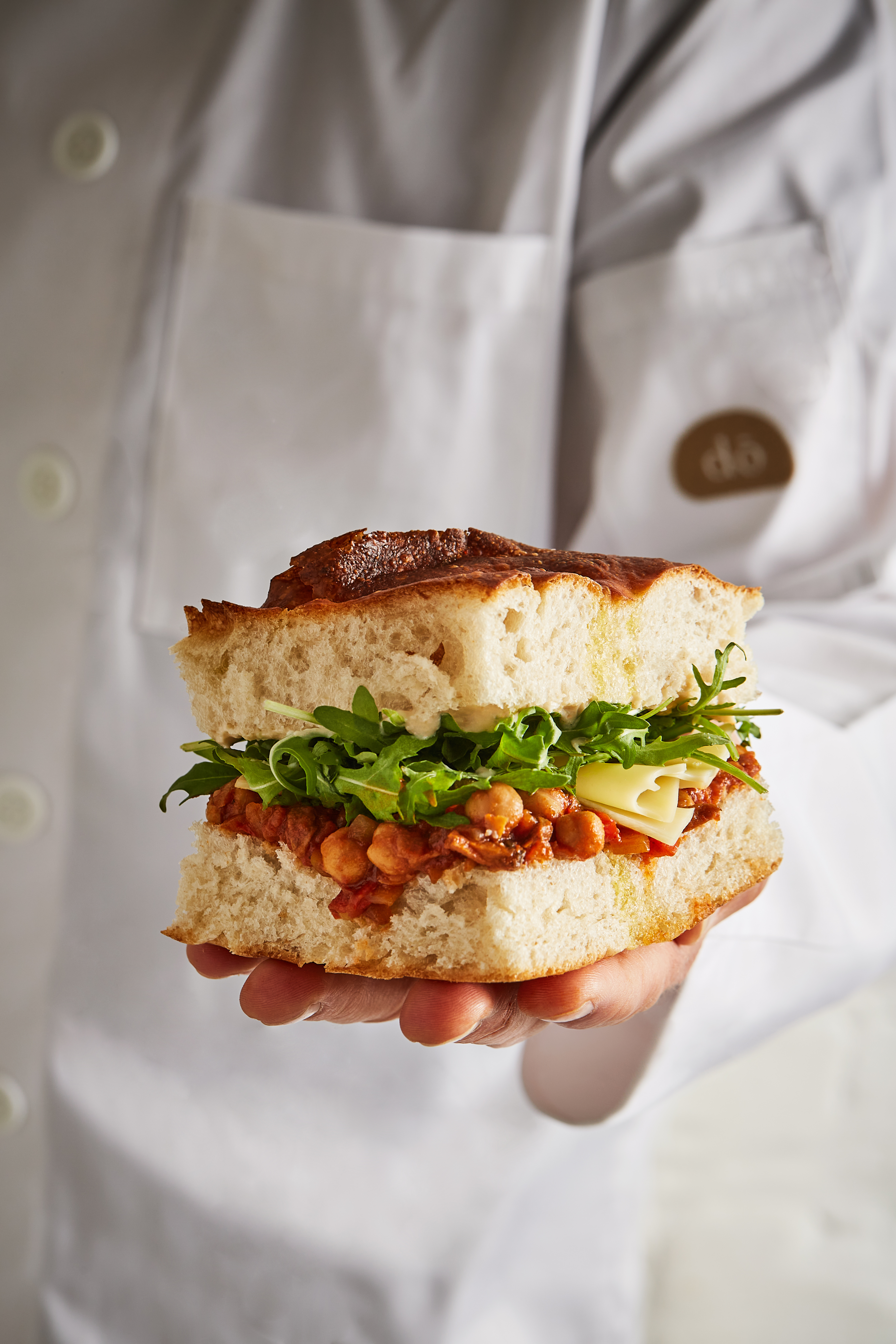 A chef proudly presents a sandwich against a clean white background, showcasing culinary expertise and creativity