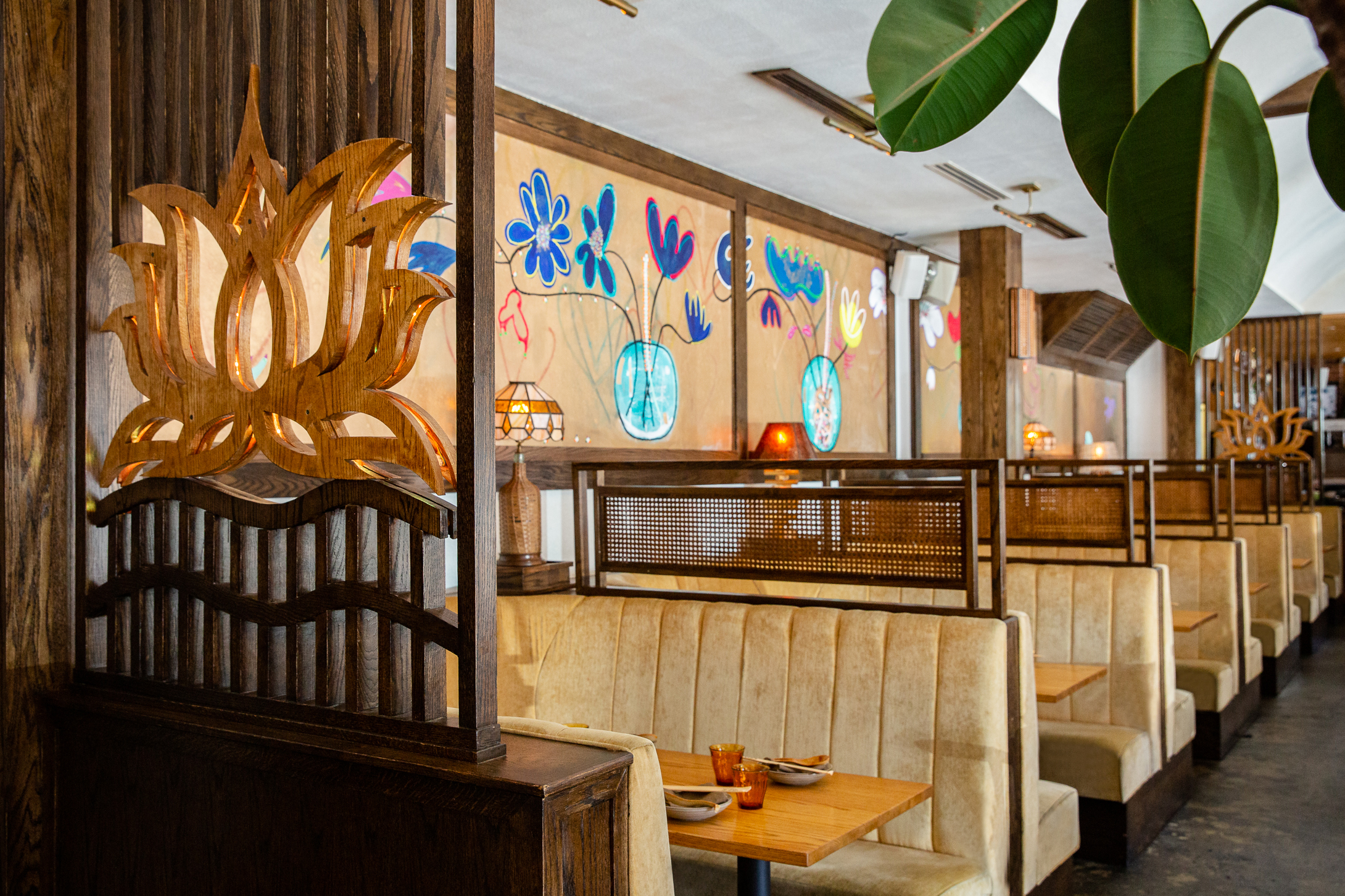 a dining room with tan banquettes and a colorful floral mural on the wall.