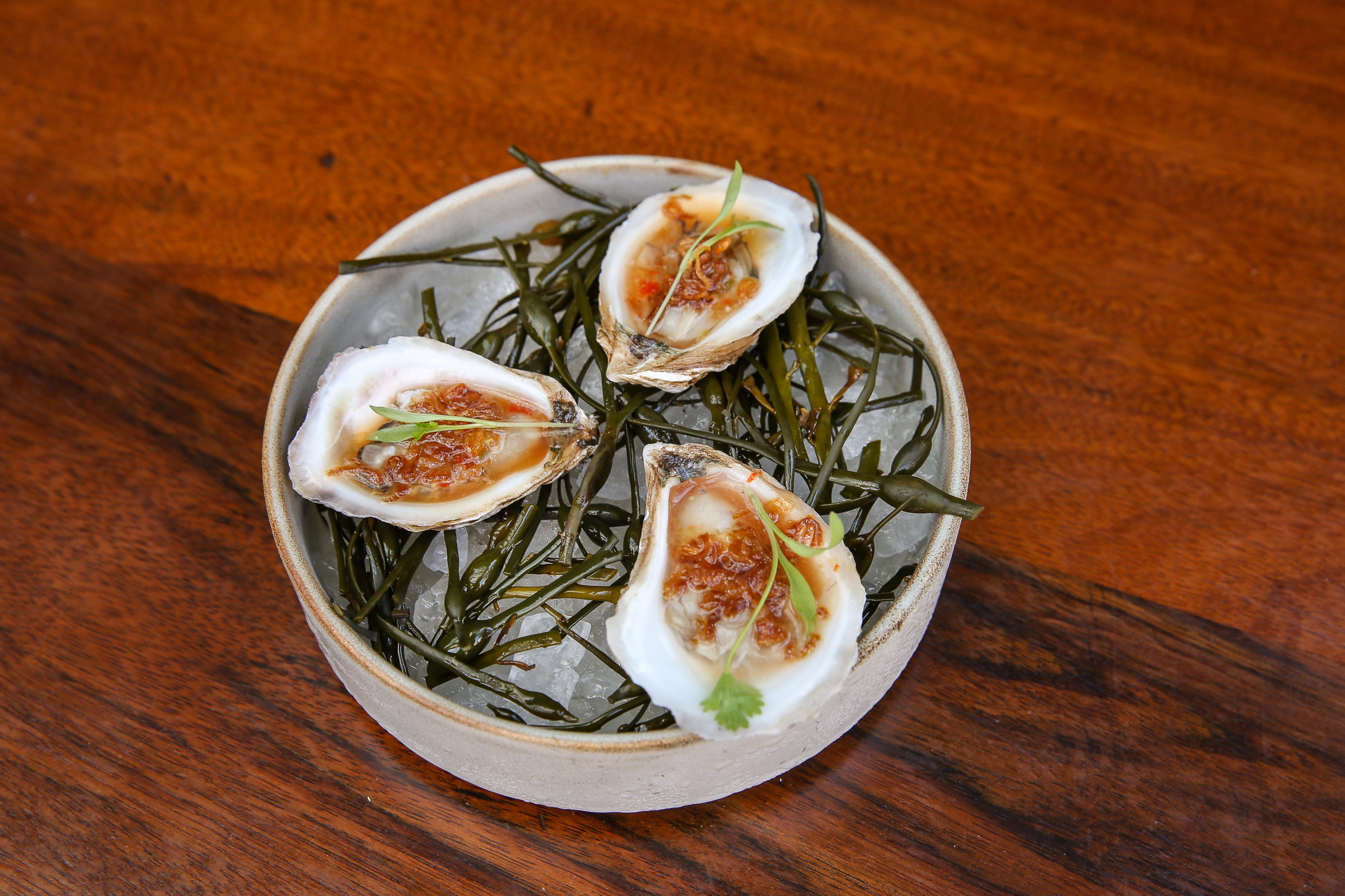 a plate of three chilled oysters with fried shallots and red chili dressing