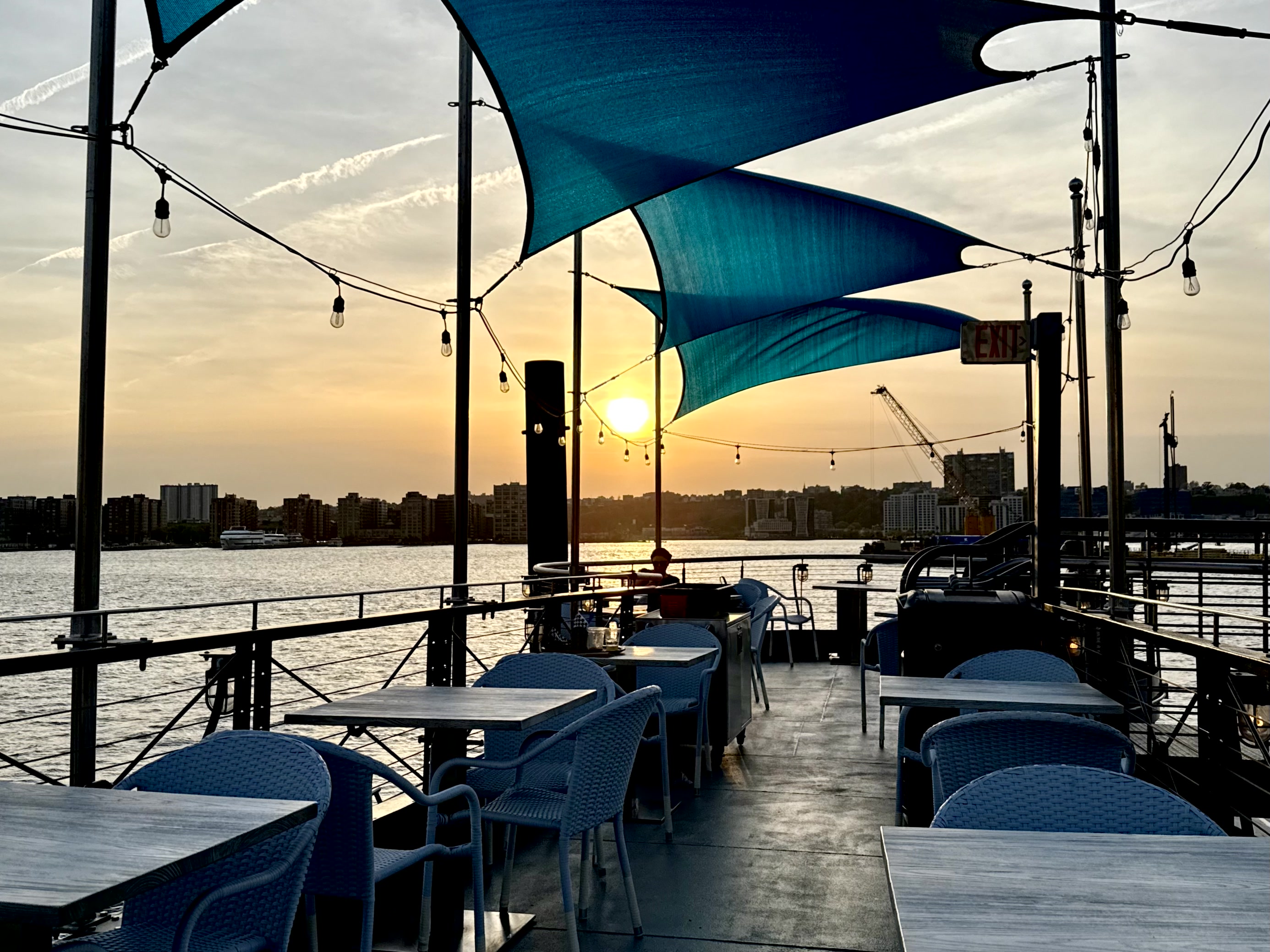 Guests eating at outdoor tables on the deck at Frying Pan NYC as a boat passes on the Hudson.