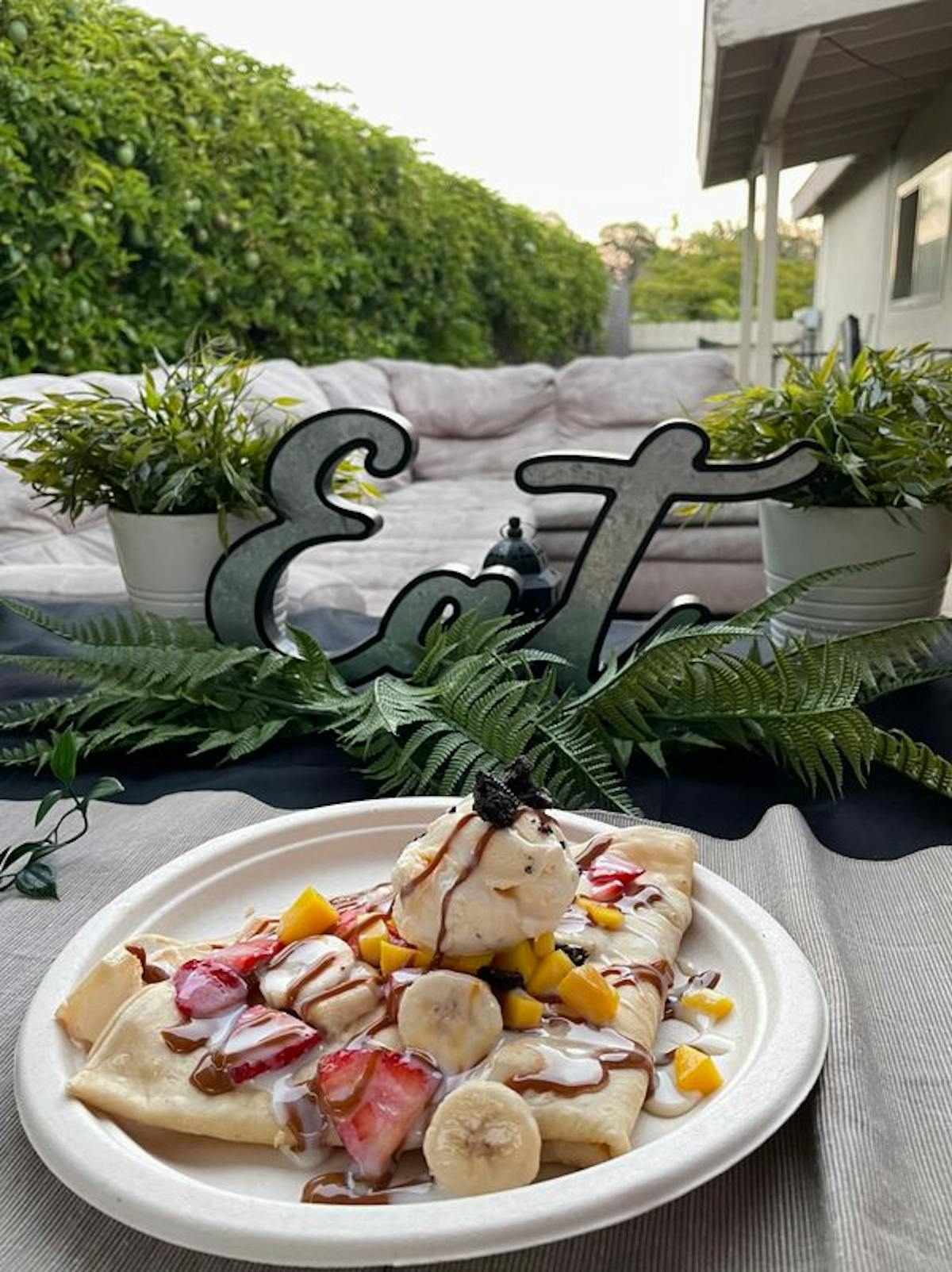 a plate of crepes topped with sliced bananas, strawberries and ice cream drizzled with chocolate