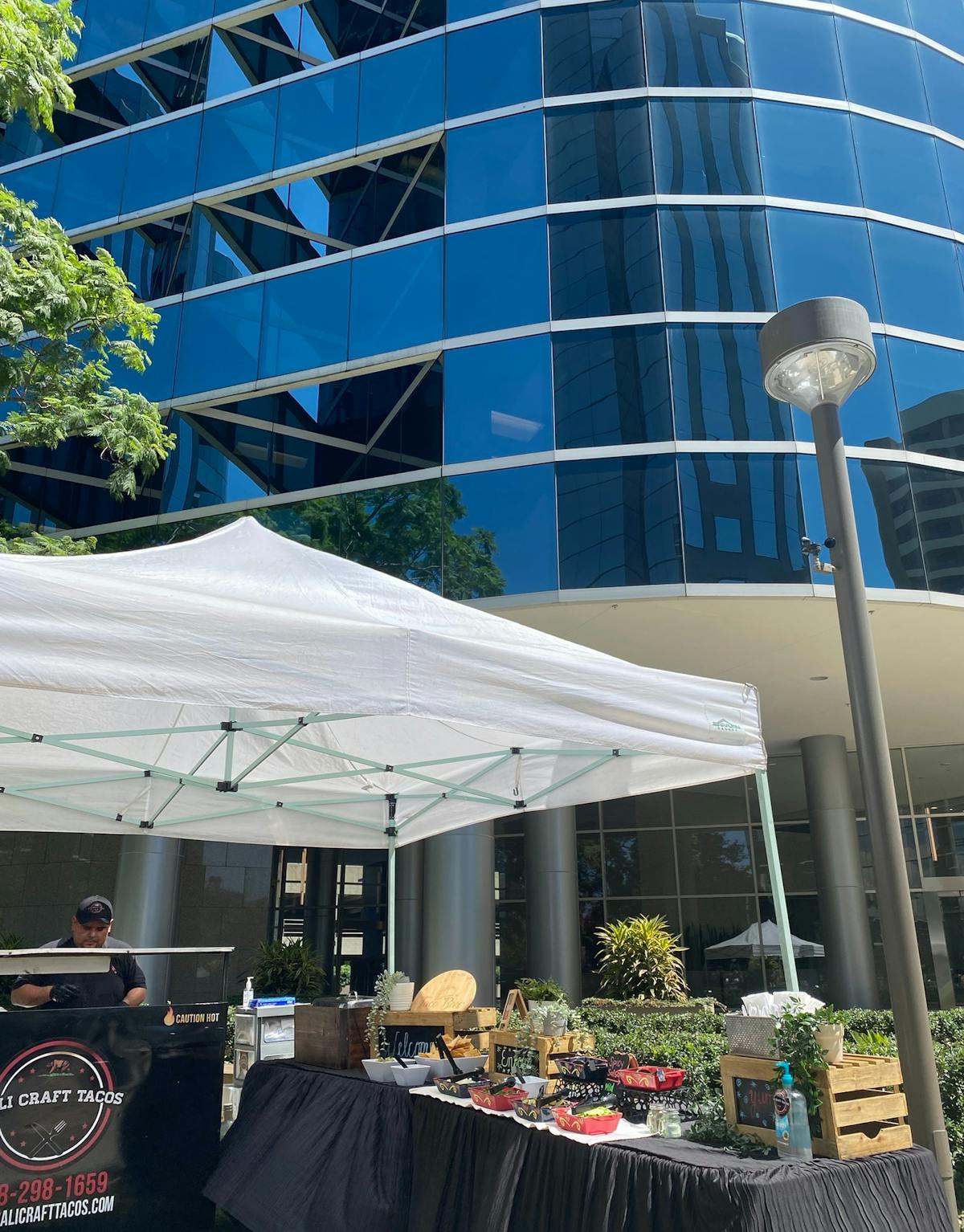 a photo of cali craft tacos food booth set up in front of a tall glass building