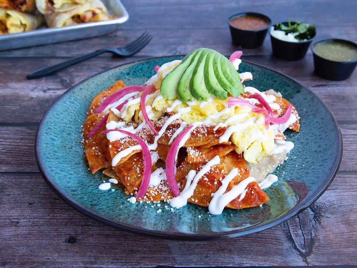 a plate of chilaquiles with slices of avocado on top 