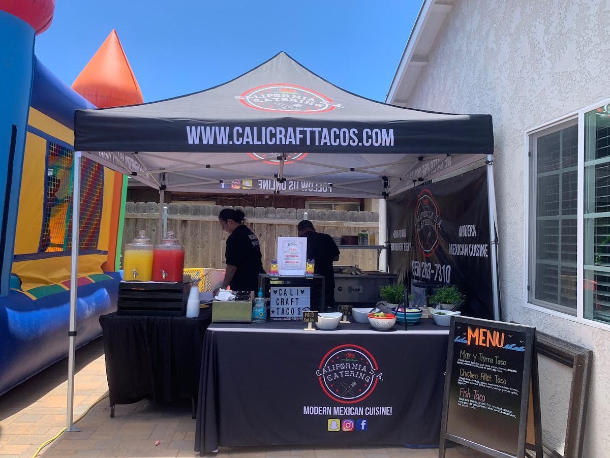 a photo of the Cali Craft taco tent setup with two people grilling and serving food