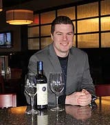 a man sitting at a table with wine glasses and smiling at the camera