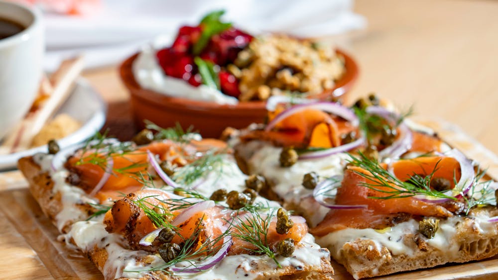 Smoked Salmon Flatbread with Labneh & Granola and a cup of coffee in the background.
