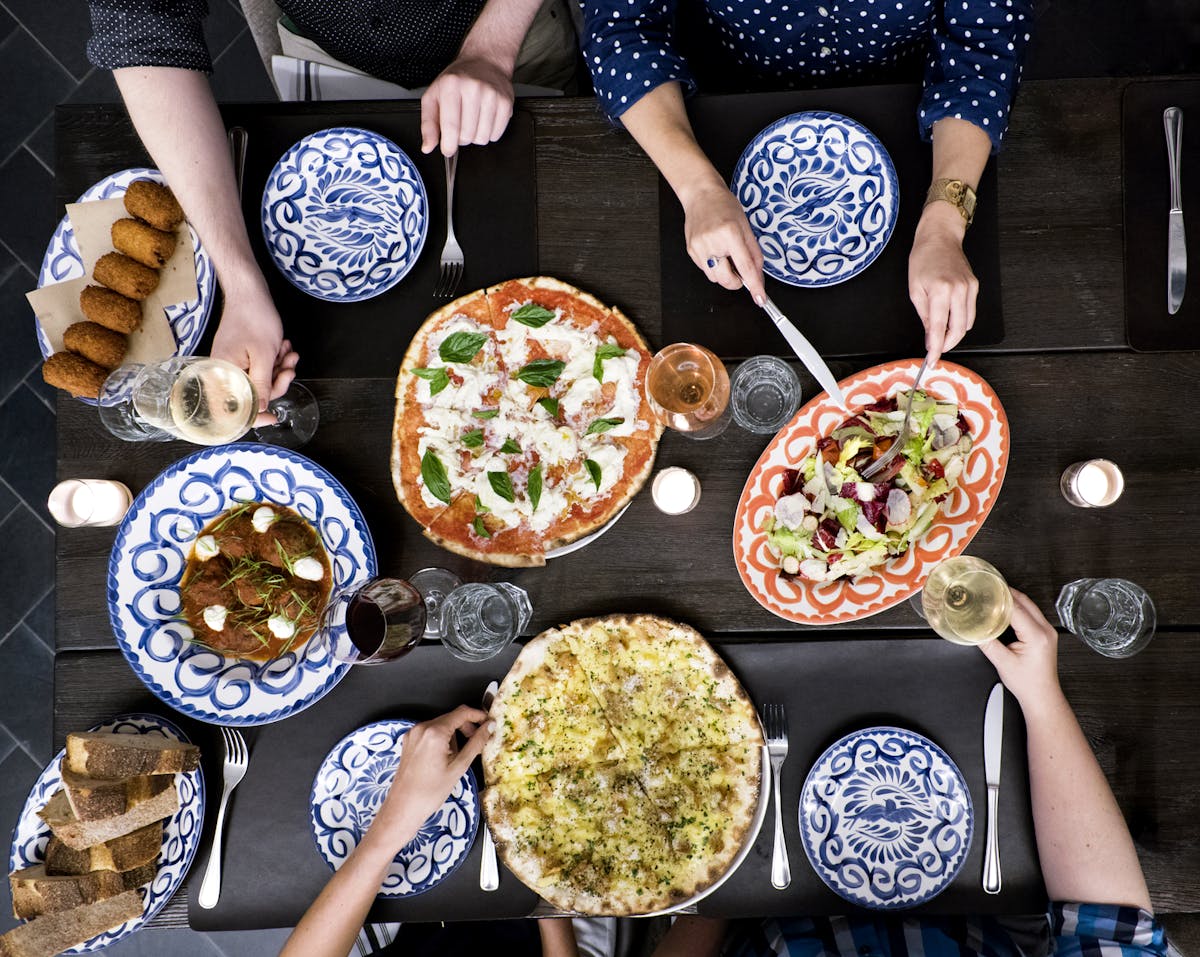 a shared table of pizzas surrounded by friends