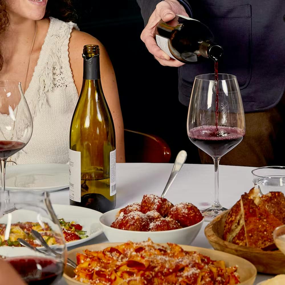 a woman sitting at a table with food and wine glasses