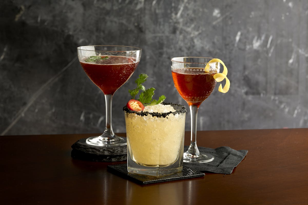 two glasses of wine and a cocktail, sitting on top of a table