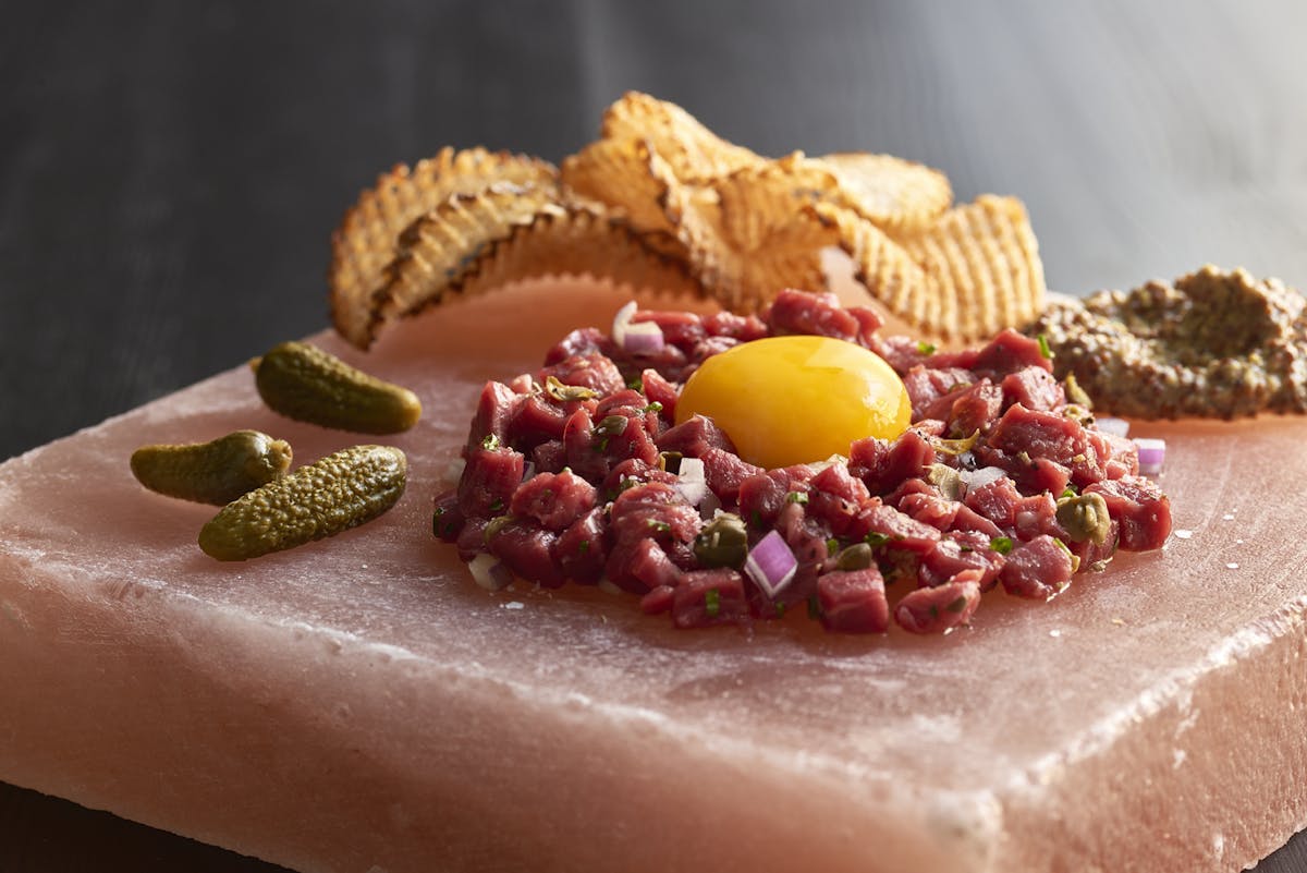 a close up of pickles, egg with cut pieces of meat, and fried potato chips