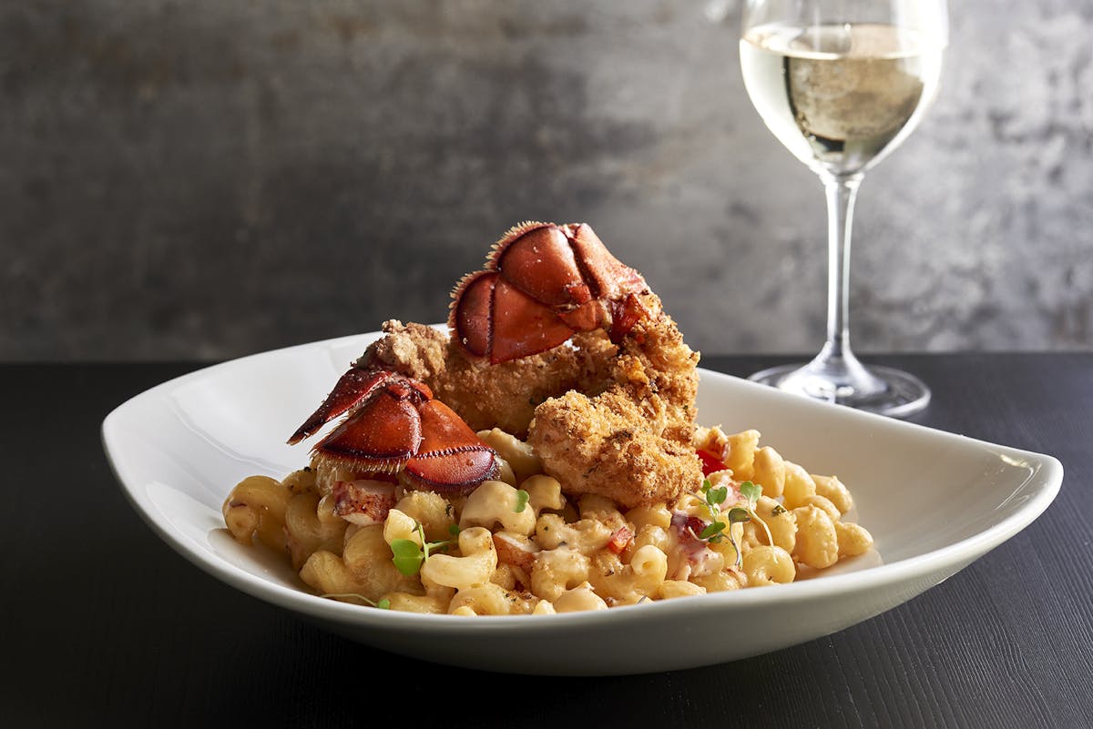 a plate of lobster and pasta with a glass of white wine