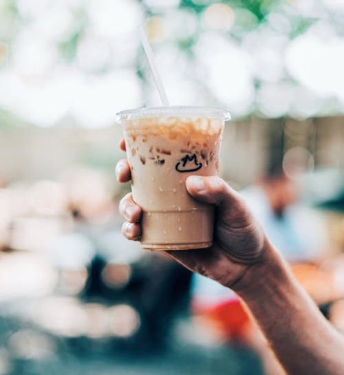 a close up of a hand holding a cup of iced coffee