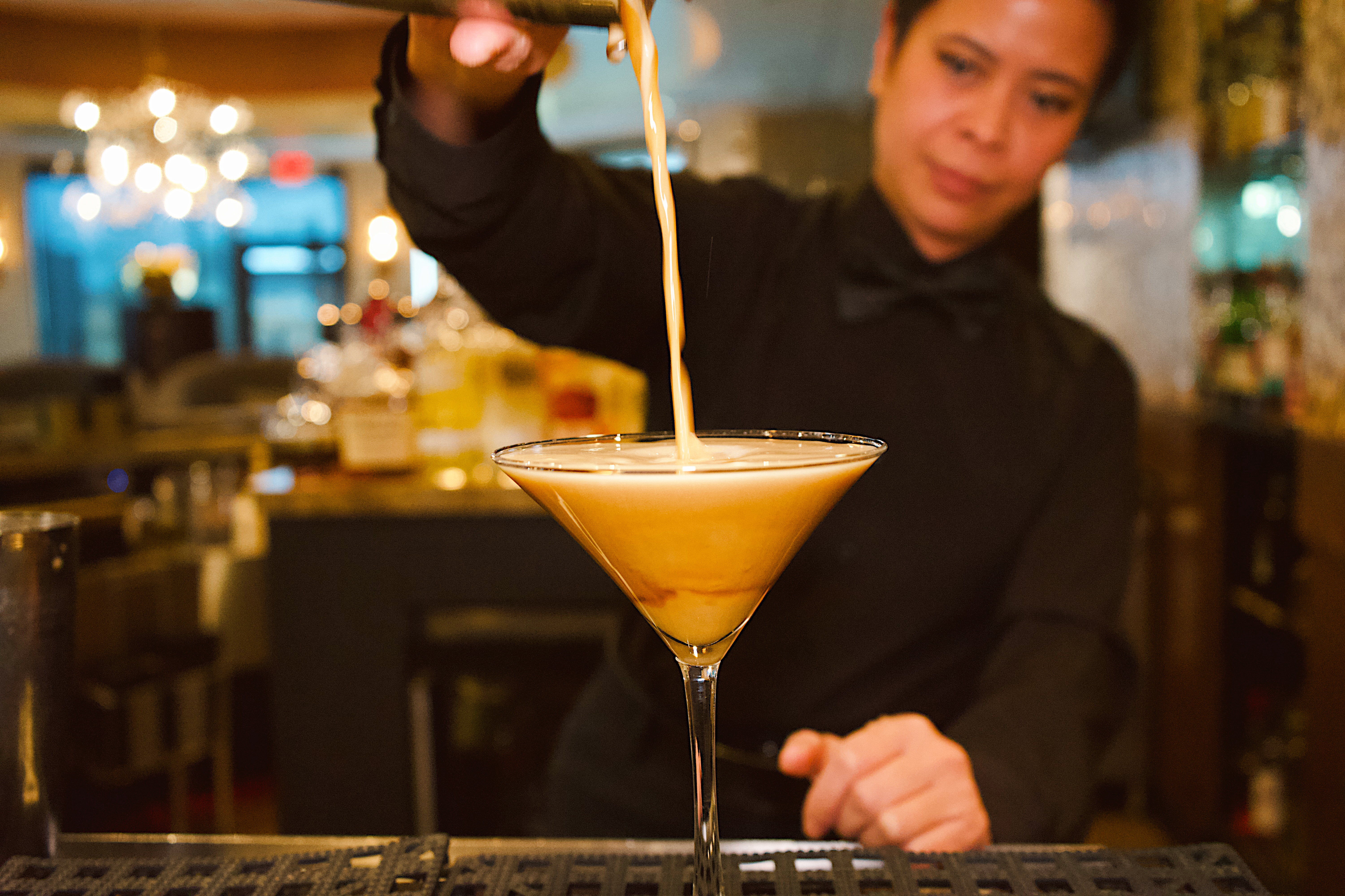 a person pouring a drink into a martini glass