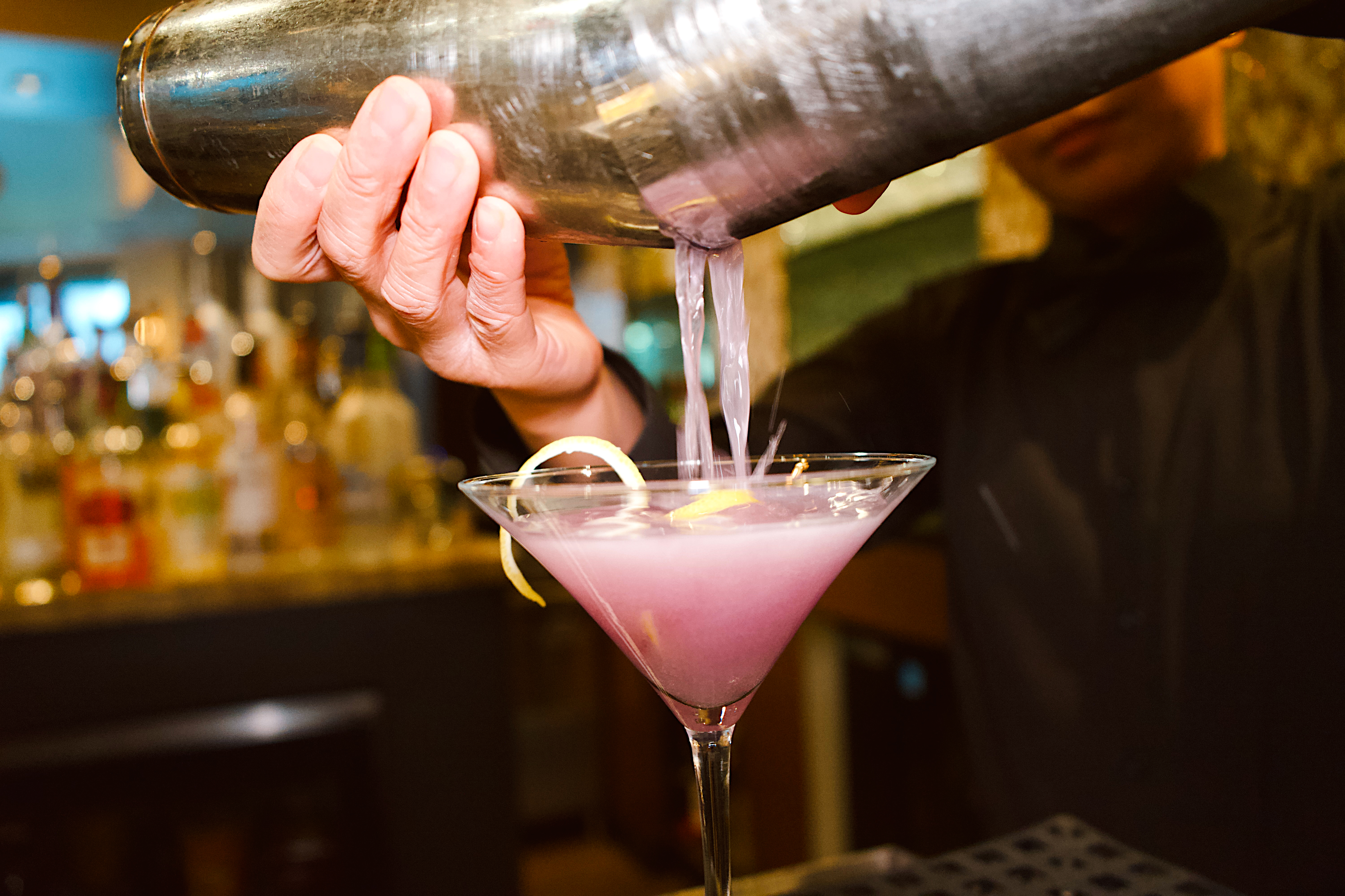 a person pouring a drink into a martini glass