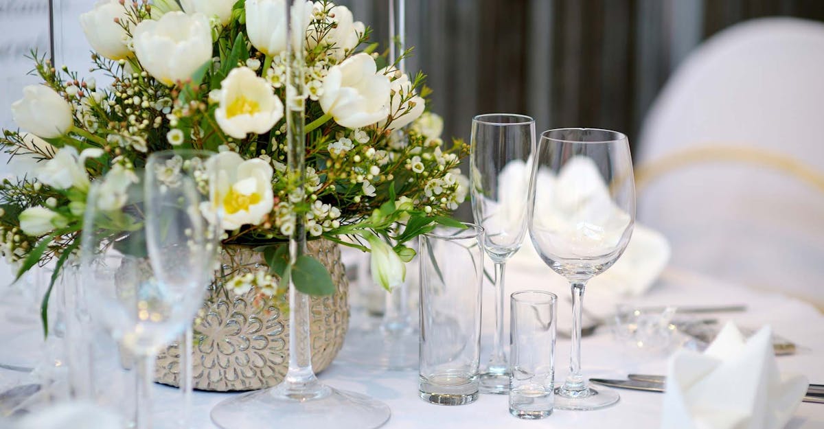 a vase of flowers on a table with wine glasses
