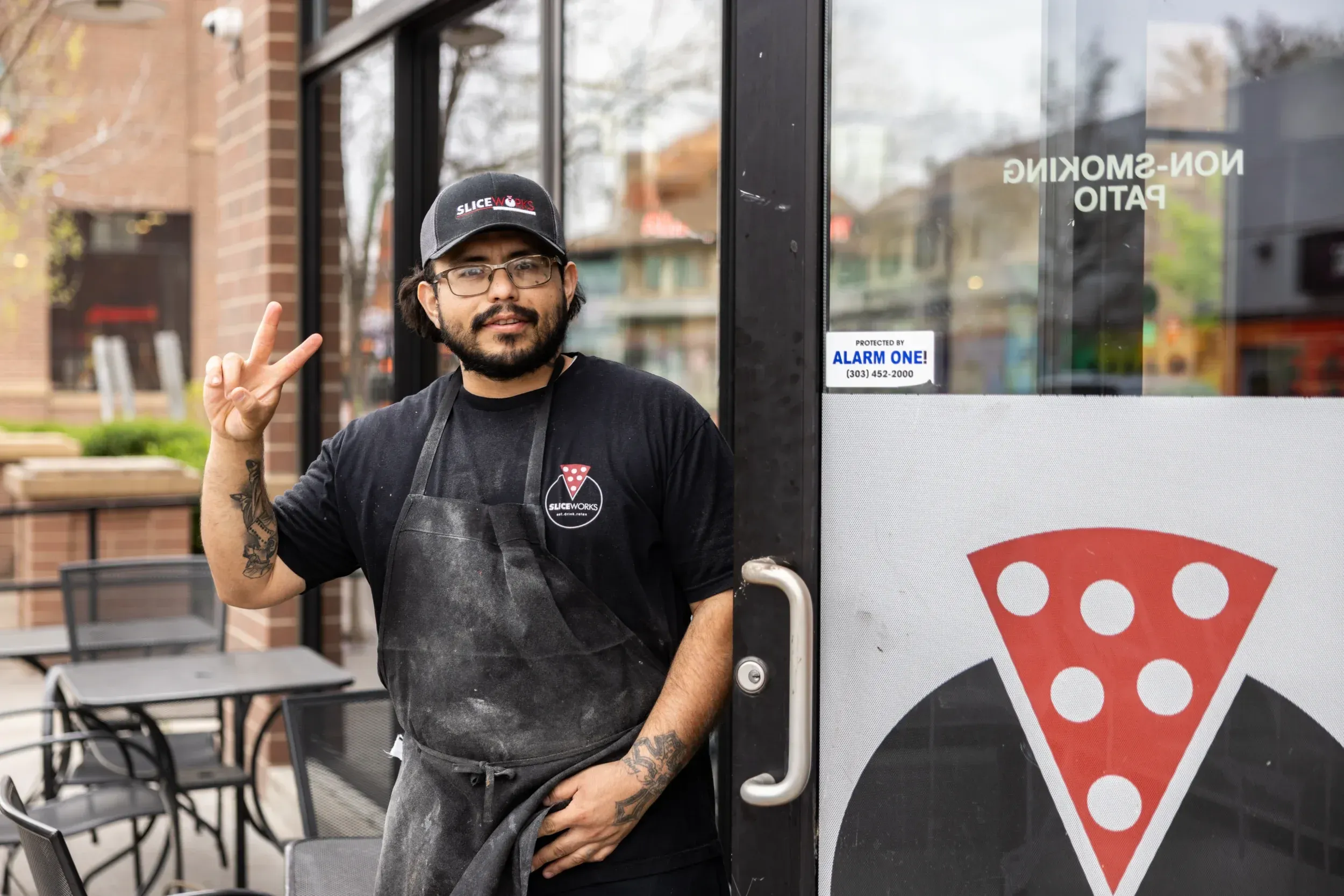 a man wearing a black apron and holding up a peace sign