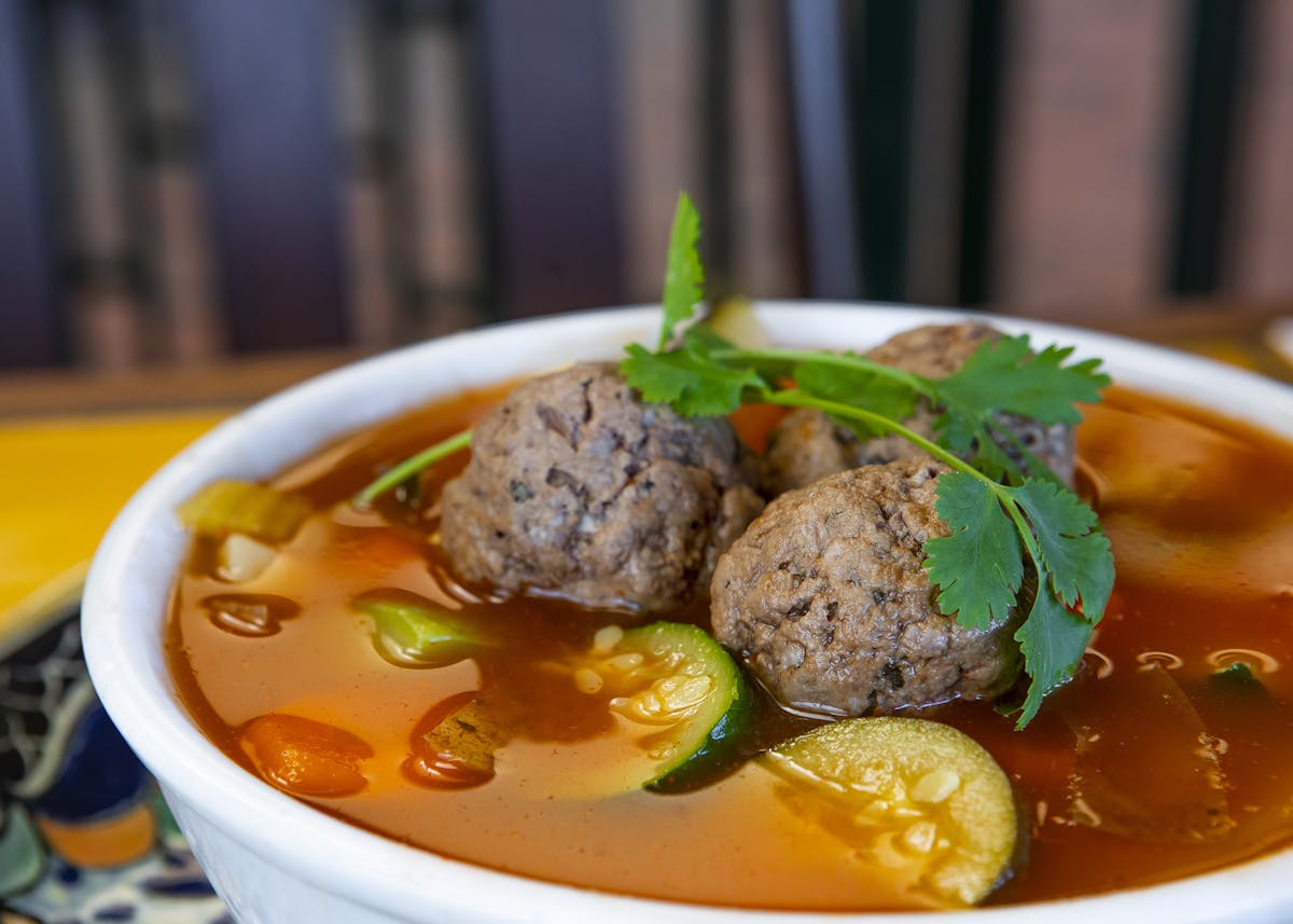 a bowl of soup with meat and vegetables on a plate