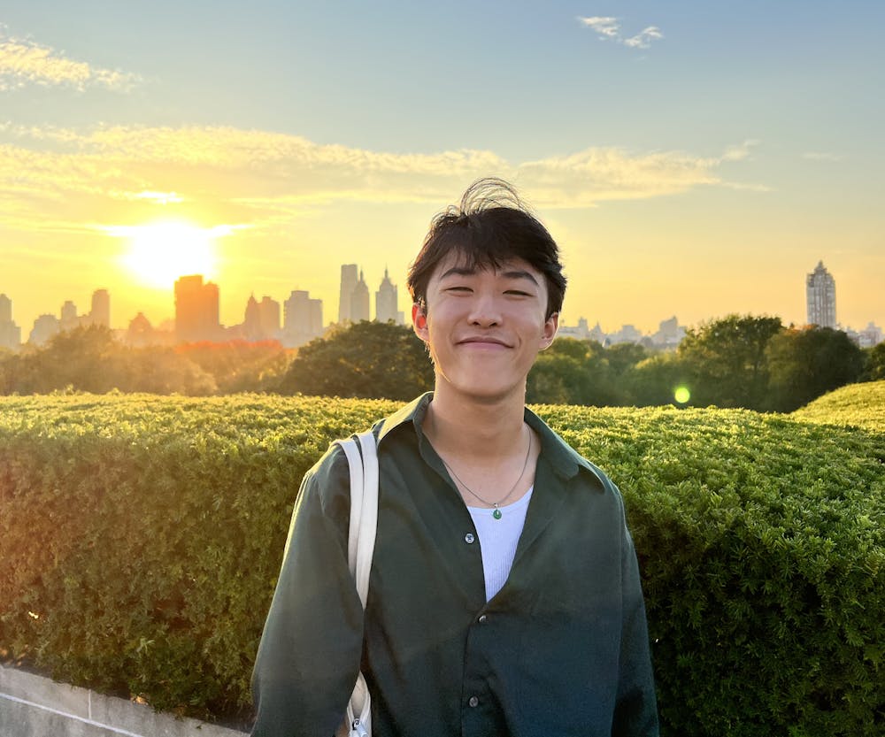 a smiling young man standing in front of a green field