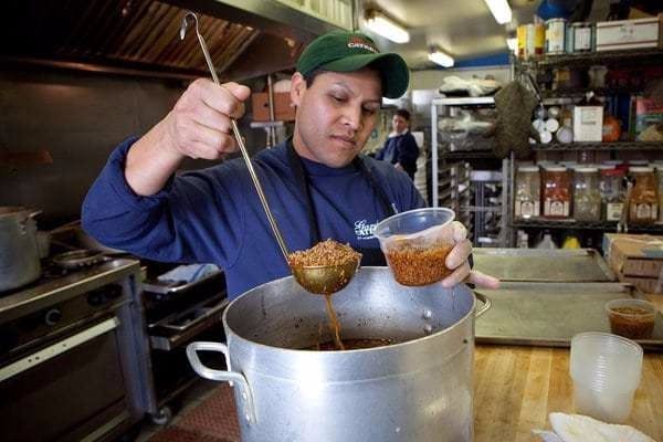 Man scooping chili into a container in a kitchen