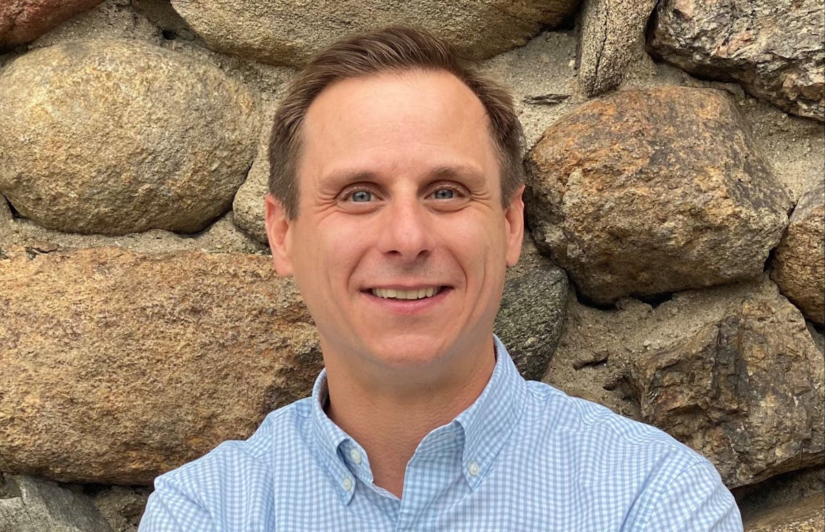 a man is smiling in front of a large rock