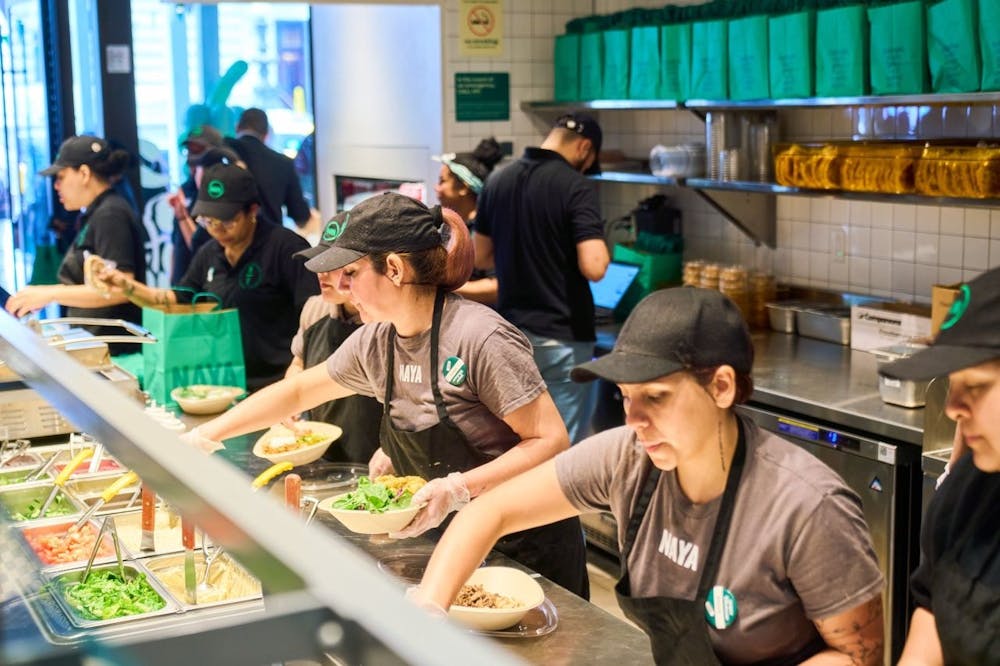 Naya team members serving salad at Naya's Bryant Park location. In frame is lettuce and other veggie toppings