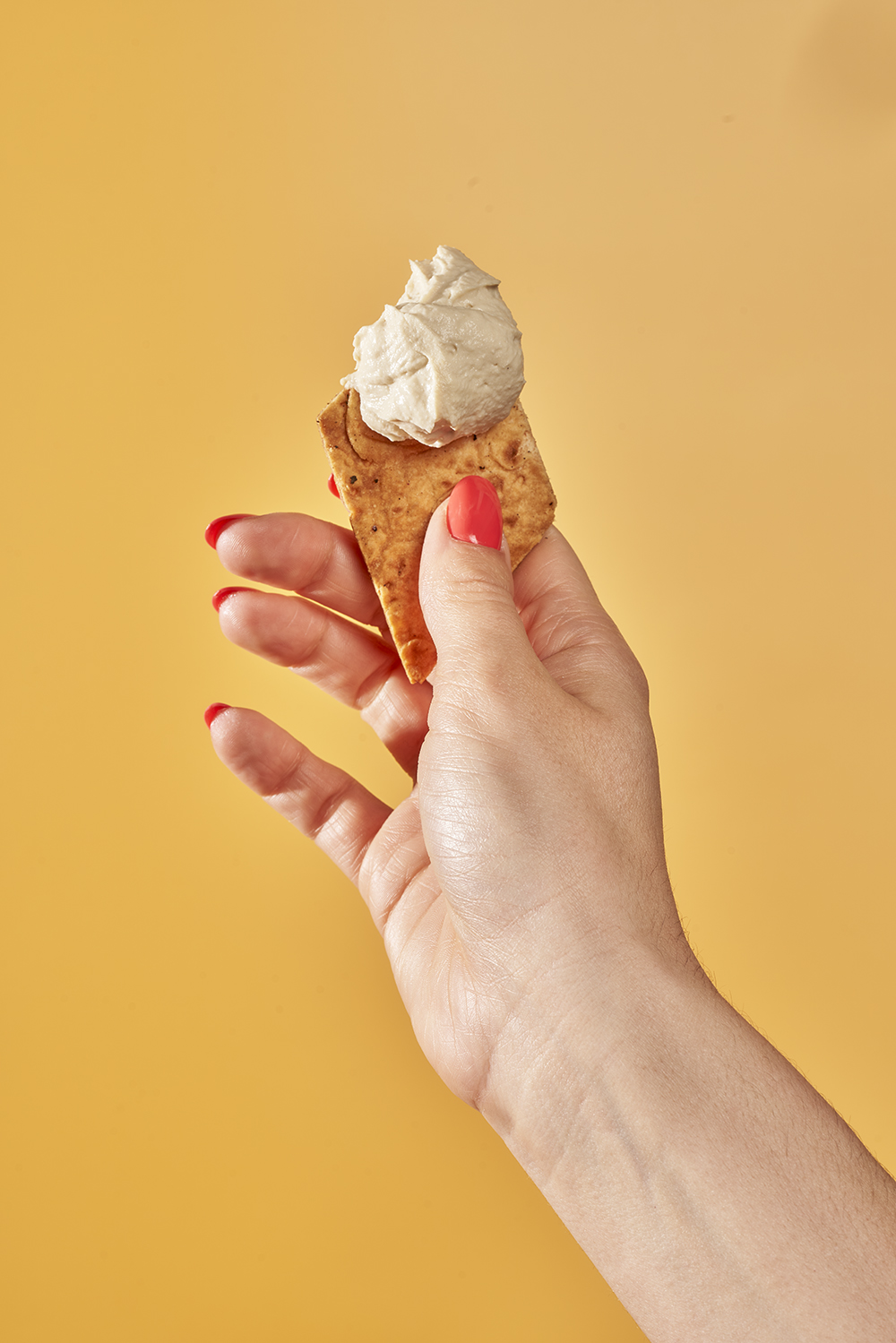 Hand holding a naya pita chip with hummus on it