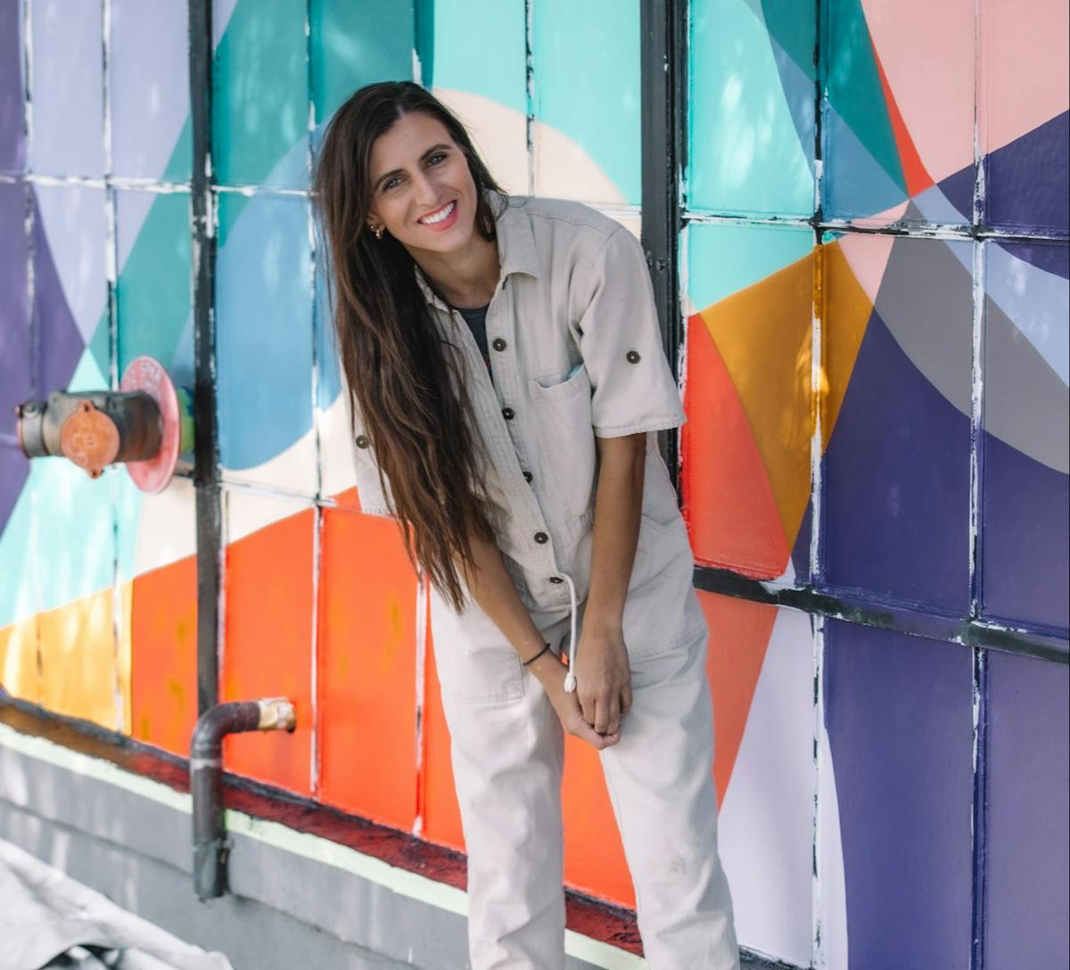 Rachel Brooks smiling and standing in front of a rainbow colored wall