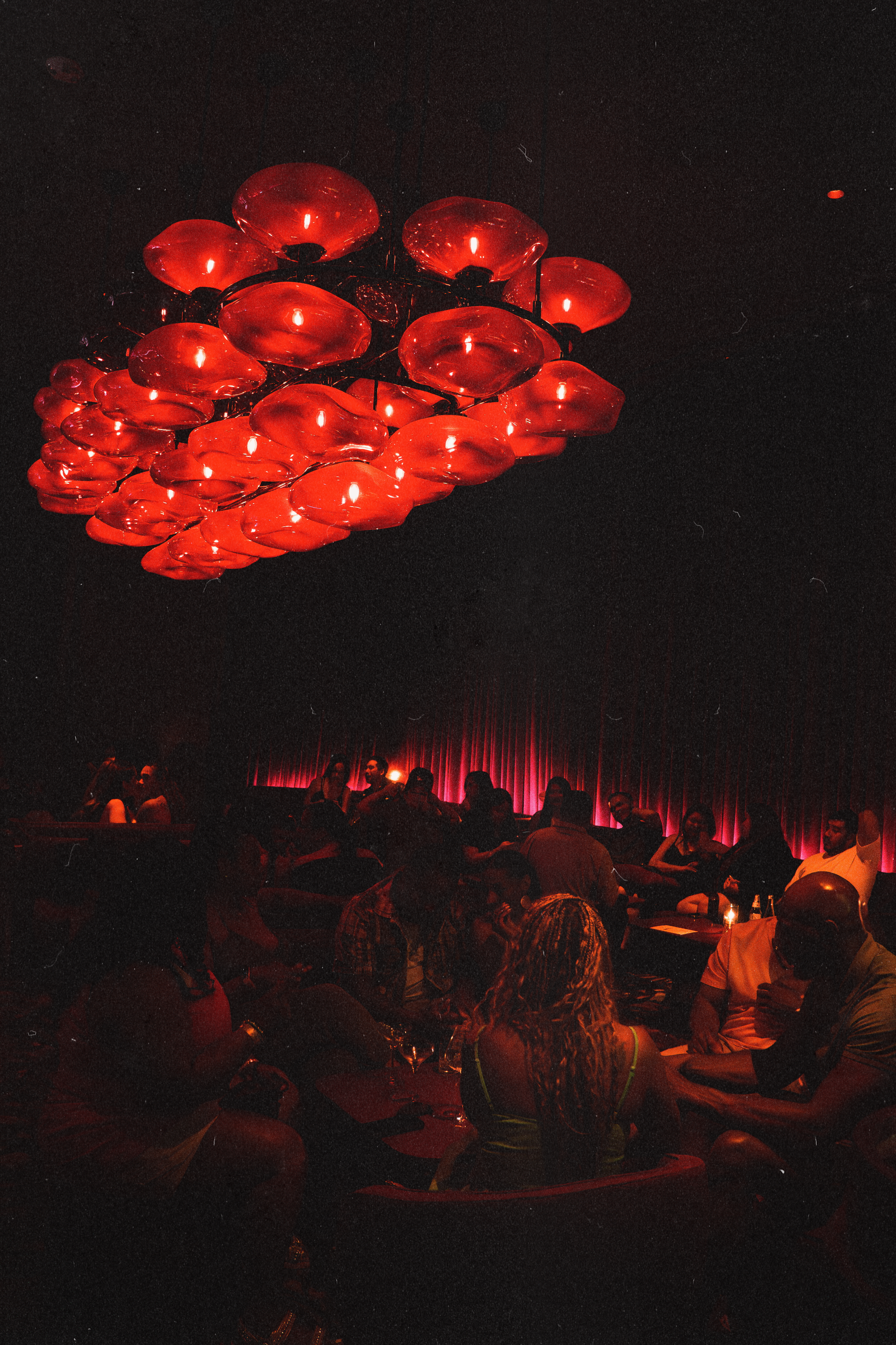 Guests enjoying cocktails and nightlife inside Wax Rabbit speakeasy beneath iconic red chandelier lighting and velvet drapery atmosphere.