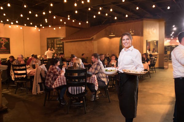 a large dining room filled with people sitting at dining tables and a waiter posing for the camera
