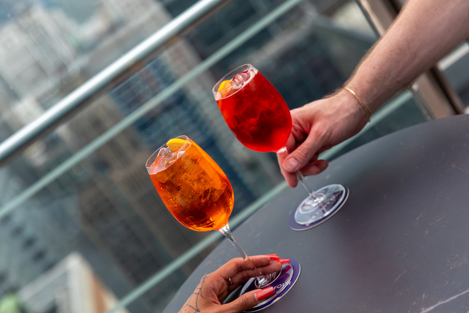 two hands holding wine glasses with orange and red liquid