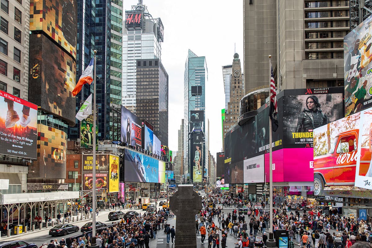 a group of people walking down a busy city street with Times Square in the background