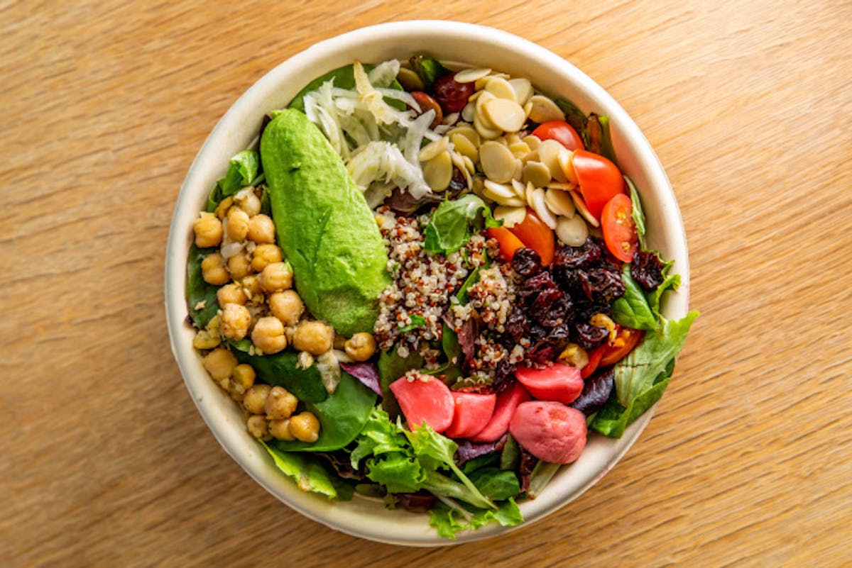a bowl of salad on a plate on a wooden table