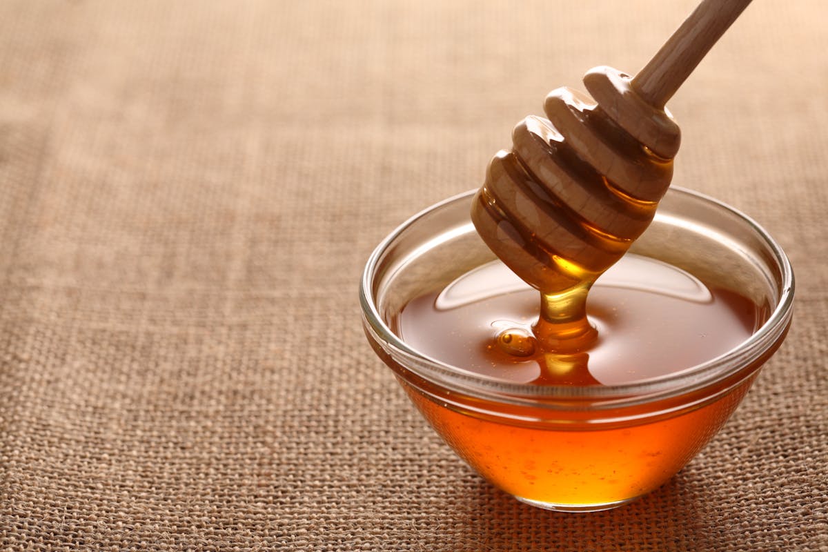 Honey dripping from honey dipper in wooden bowl. Close-up.